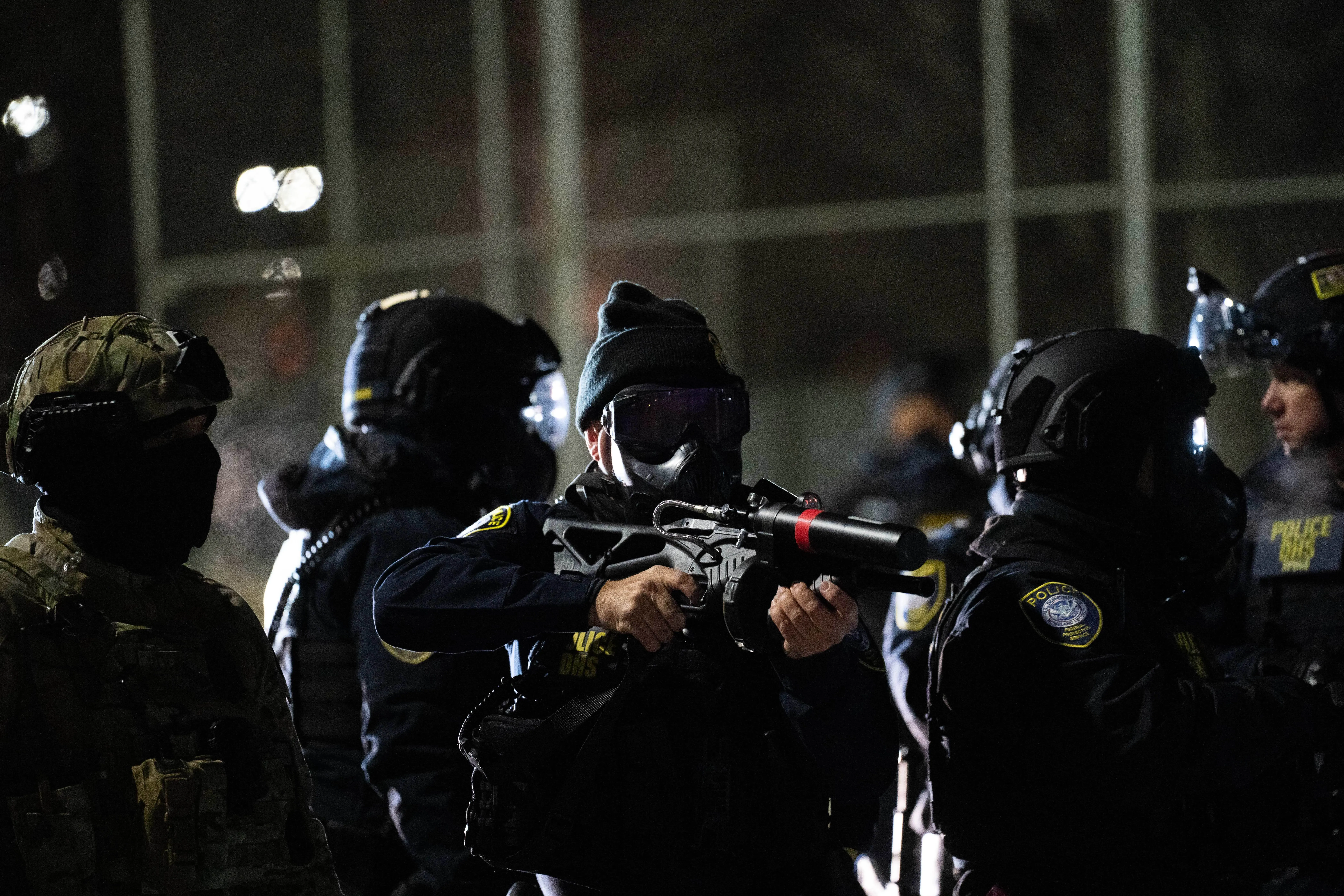 تظهر الصورة مجموعة من الضباط الفيدراليين يرتدون معدات تكتيكية، بعضهم يحمل أسلحة غير قاتلة، خلال احتجاجات في مينيابوليس ضد قوانين الهجرة.