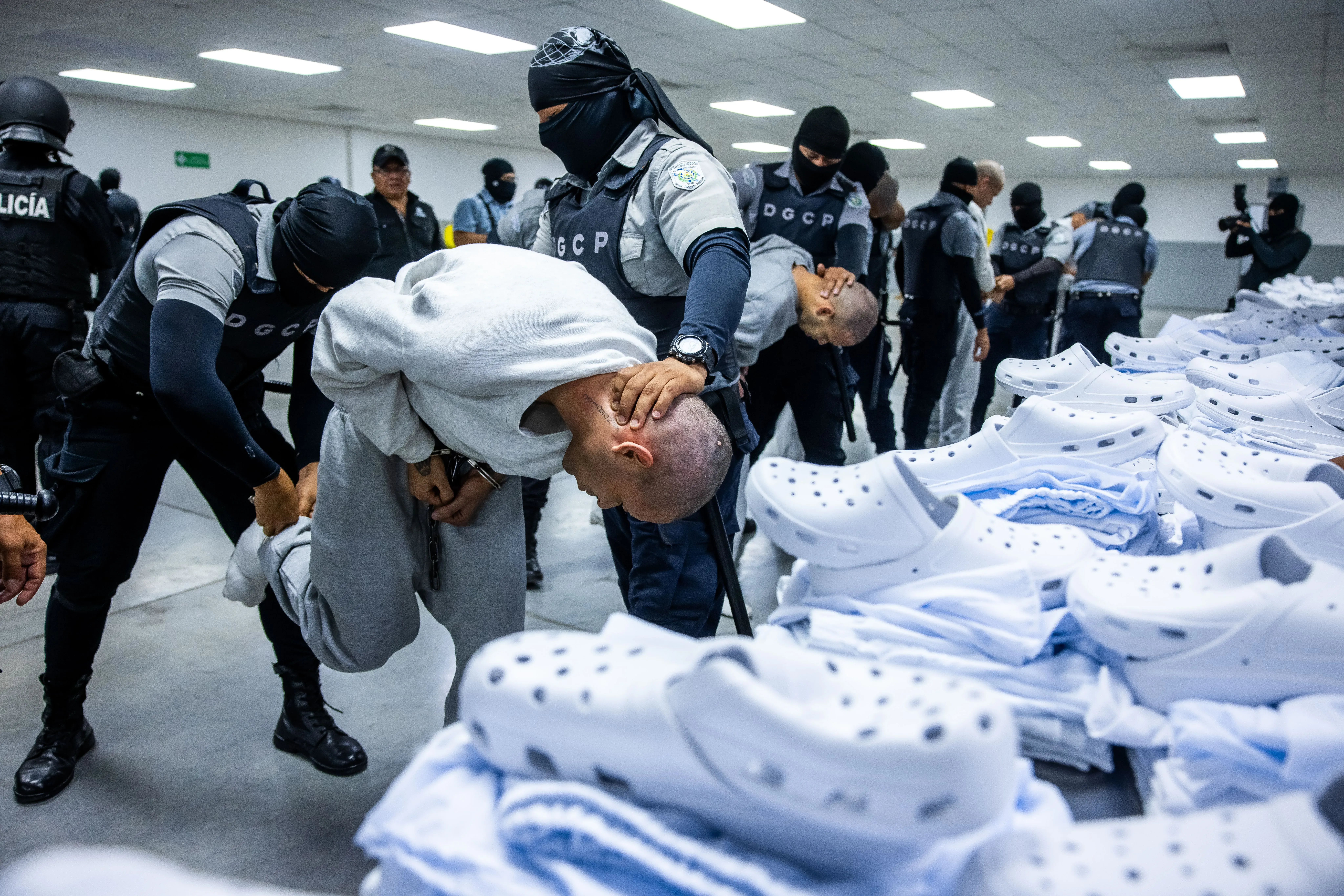 اعتقال فنزويليين في سجن سيكوت بالسلفادور، حيث يتعرضون للعنف والتعذيب على يد الحراس، مع وجود أعداد كبيرة من الأحذية البيضاء في الخلفية.