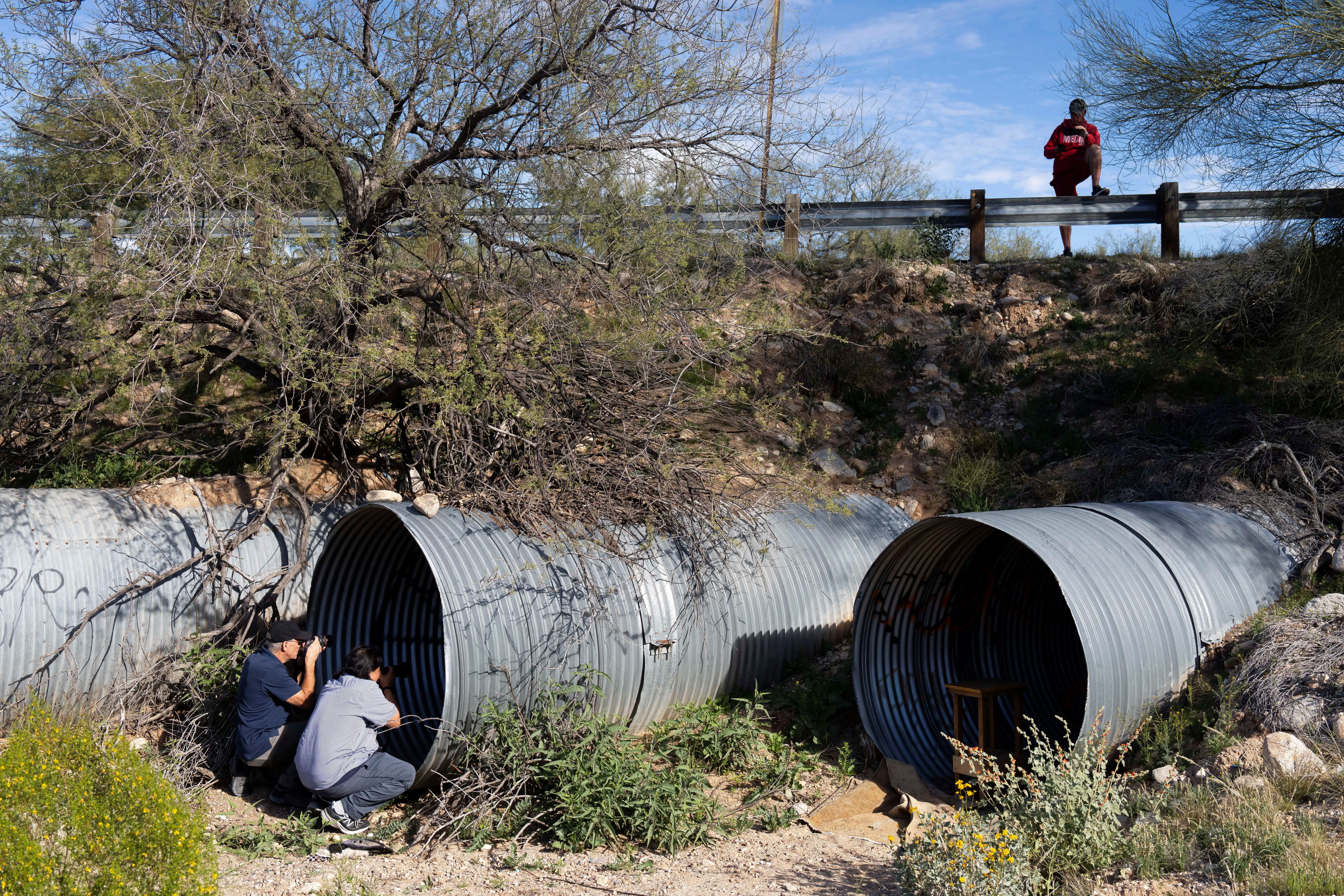 شخصان يستكشفان أنفاقًا معدنية في منطقة صحراوية، بينما يقف شخص ثالث على حافة الطريق. تعكس الصورة جهود البحث عن نانسي غوثري المفقودة.