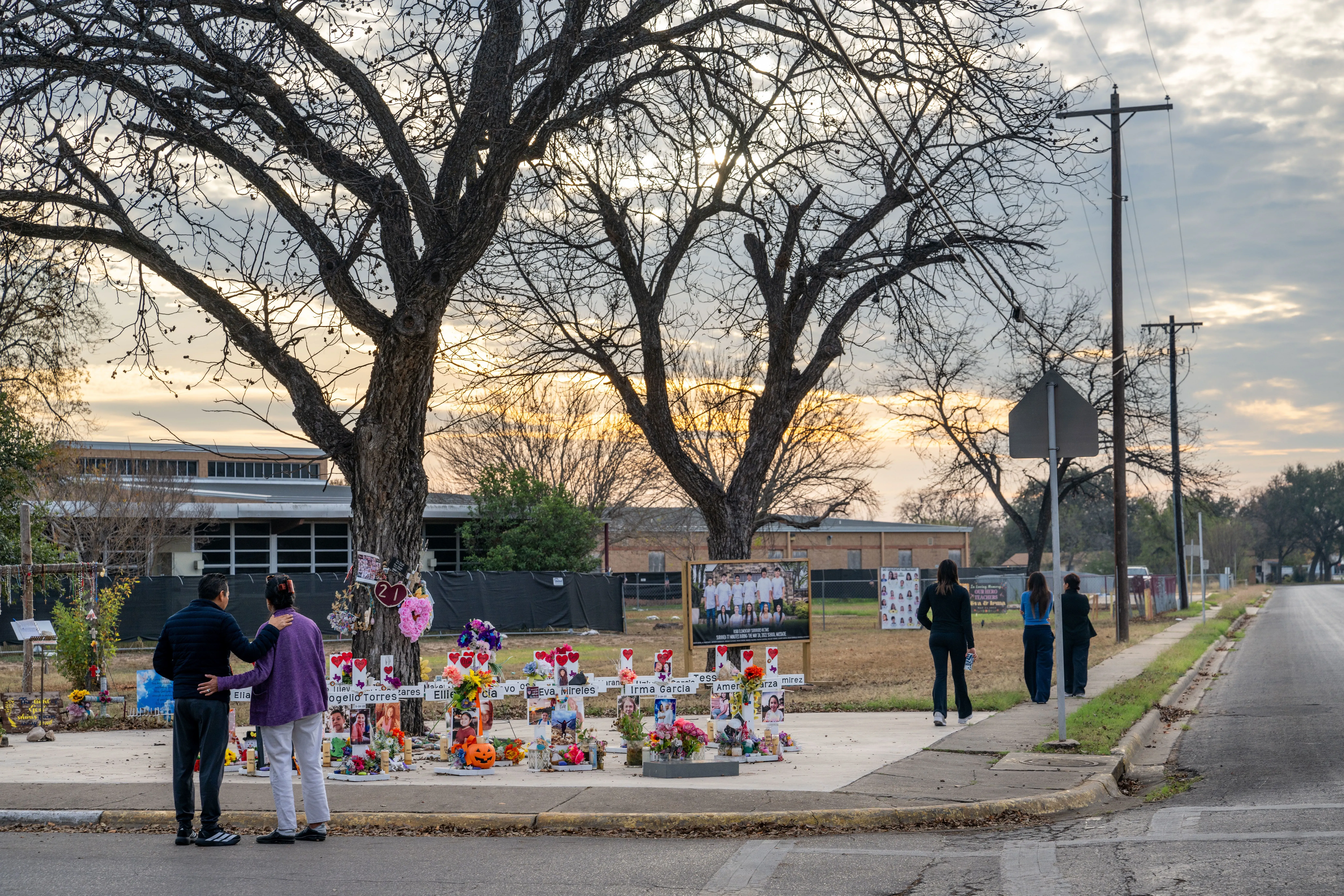 موقع تذكاري في أوفالدي، تكساس، حيث يقف زوار أمام صور وضعت تكريمًا لضحايا مذبحة مدرسة روب الابتدائية، مع أجواء حزينة في الخلفية.
