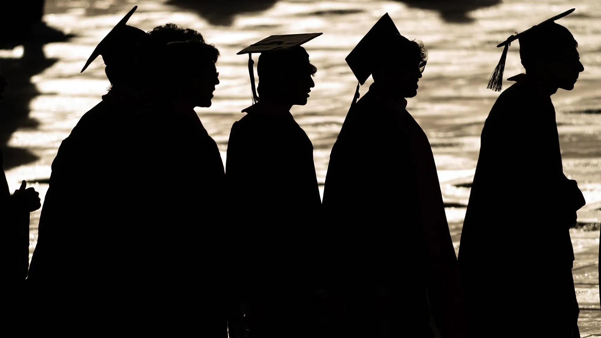 تظهر الصورة silhouettes لطلبة خريجين يرتدون قبعات التخرج، مما يعكس التحديات التي يواجهها خريجو علوم الكمبيوتر في سوق العمل.