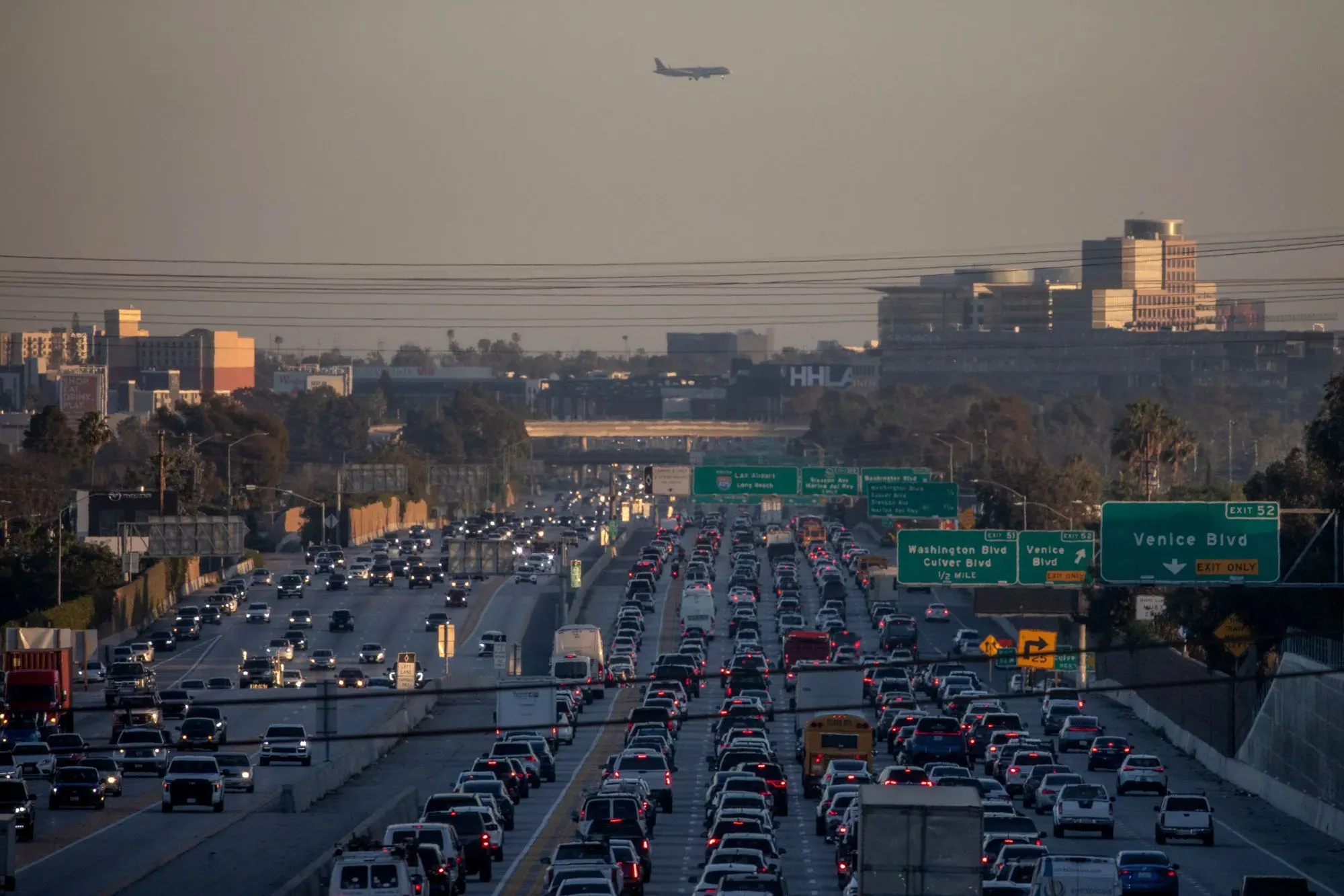 ازدحام مروري كثيف على طريق سريع في مدينة كبيرة، مع طائرة تحلق في السماء، مما يبرز تأثير النقل على التلوث البيئي.