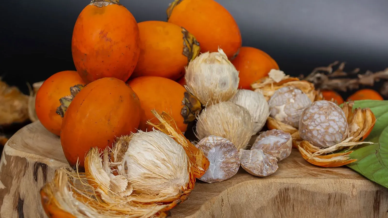 صورة تظهر مجموعة من ثمار جوز التنبول، بعضها مقشر وبعضها الآخر غير مقشر، موضوعة على قطعة خشبية، تعكس الاستخدام التاريخي للمكسرات في الثقافات القديمة.