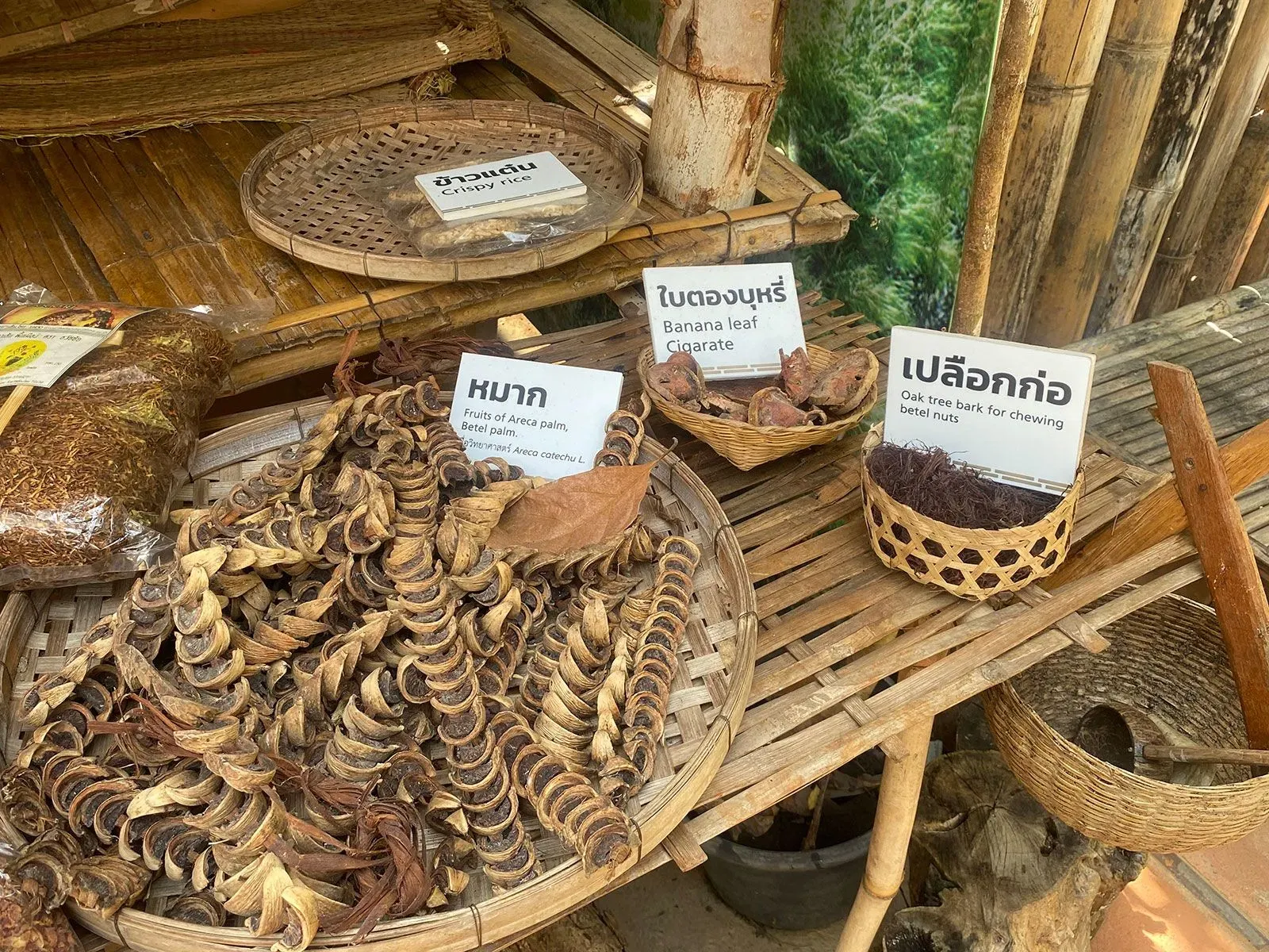 تظهر الصورة مجموعة من المكونات التقليدية المستخدمة في تحضير مكسرات التنبول، بما في ذلك جوز التنبول وقشور الأشجار، مع لافتات توضح الأسماء.