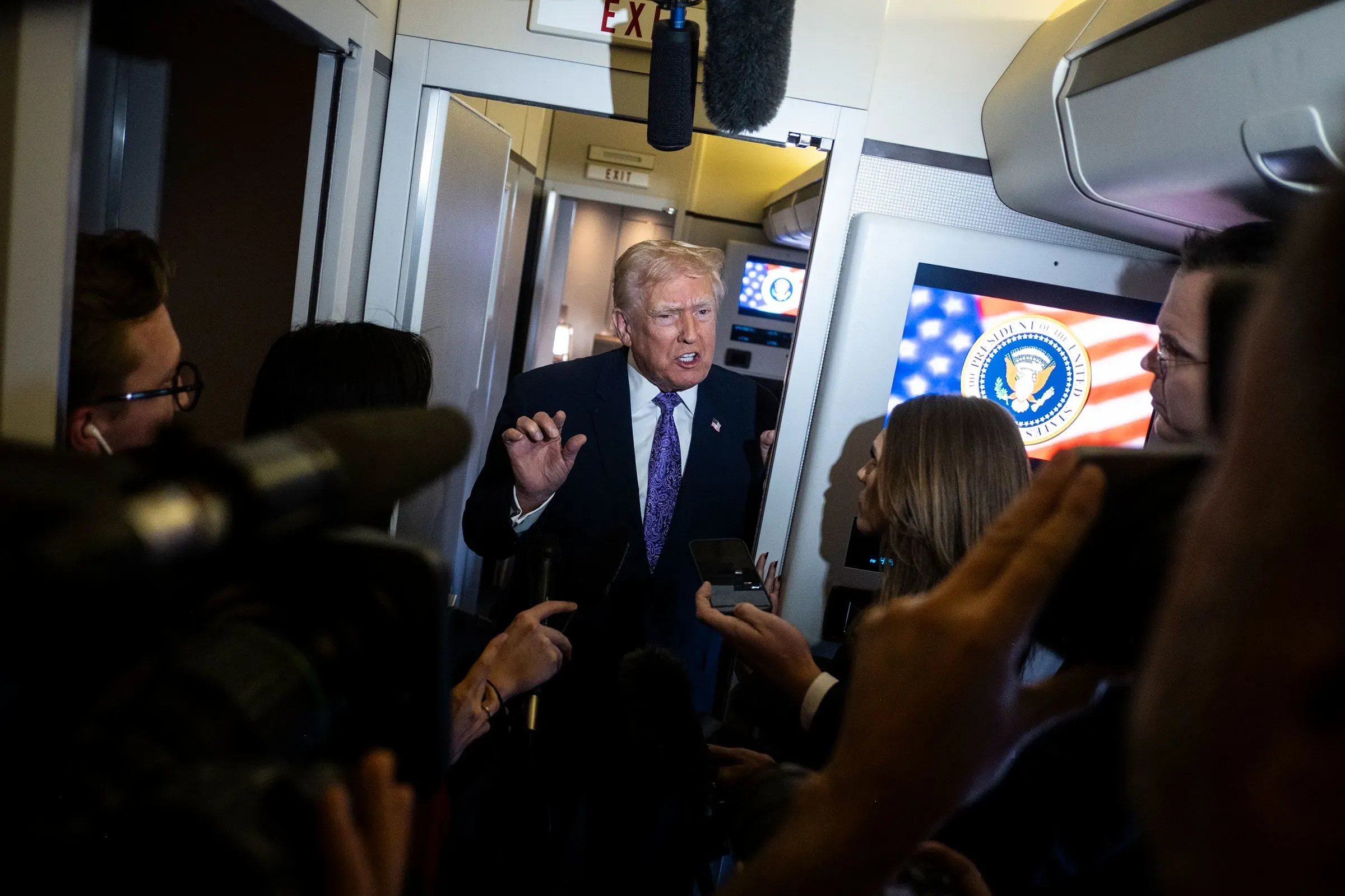 ترامب يتحدث للصحفيين داخل الطائرة الرئاسية، محاطاً بكاميرات وميكروفونات، في سياق انتقادات حول الهجمات العسكرية.