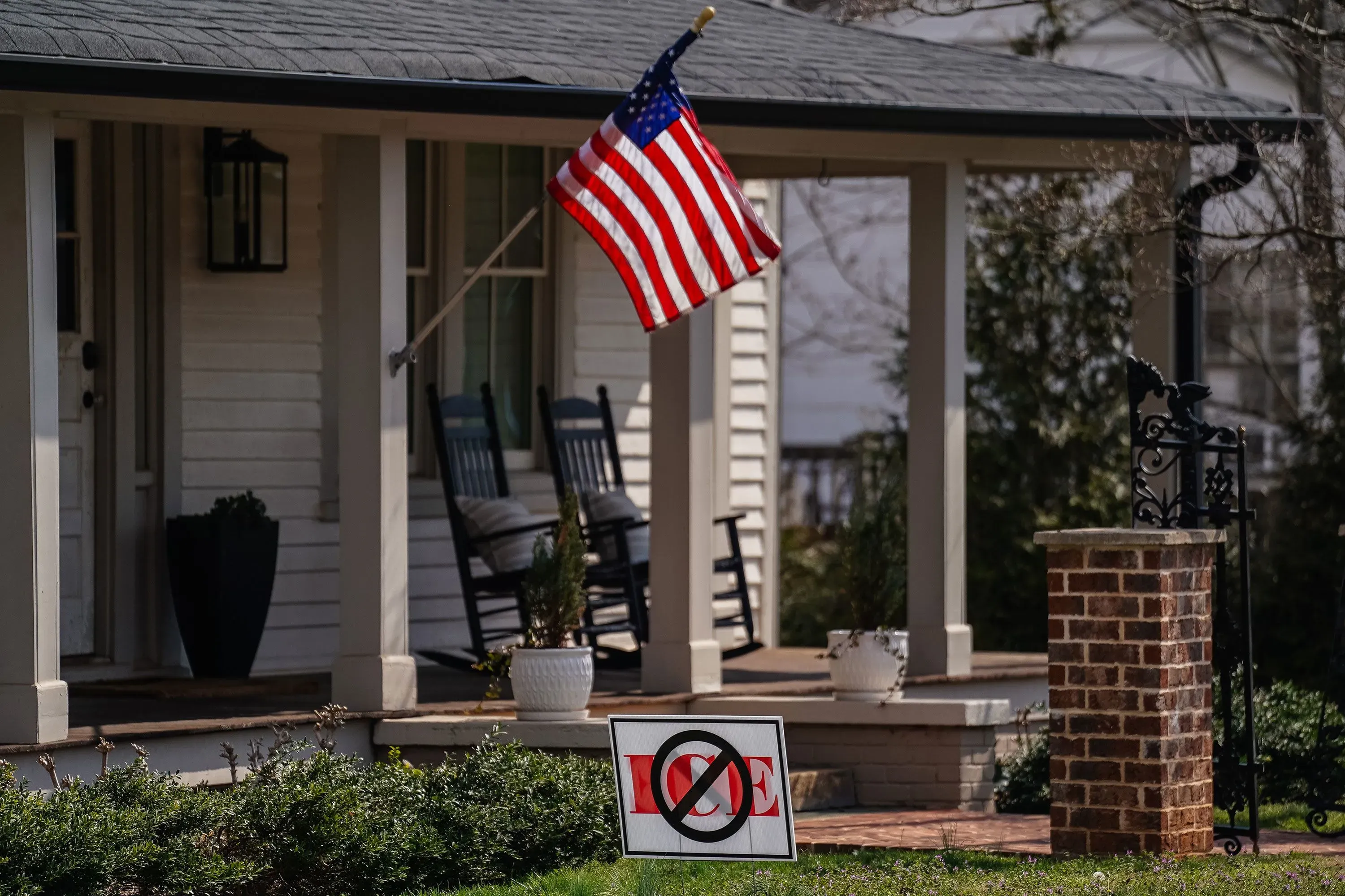 علم أمريكي يرفرف أمام منزل، مع لافتة تحذر من عدم الترحيب بالمهاجرين، تعكس مشاعر معارضة لسياسات الهجرة الحالية.