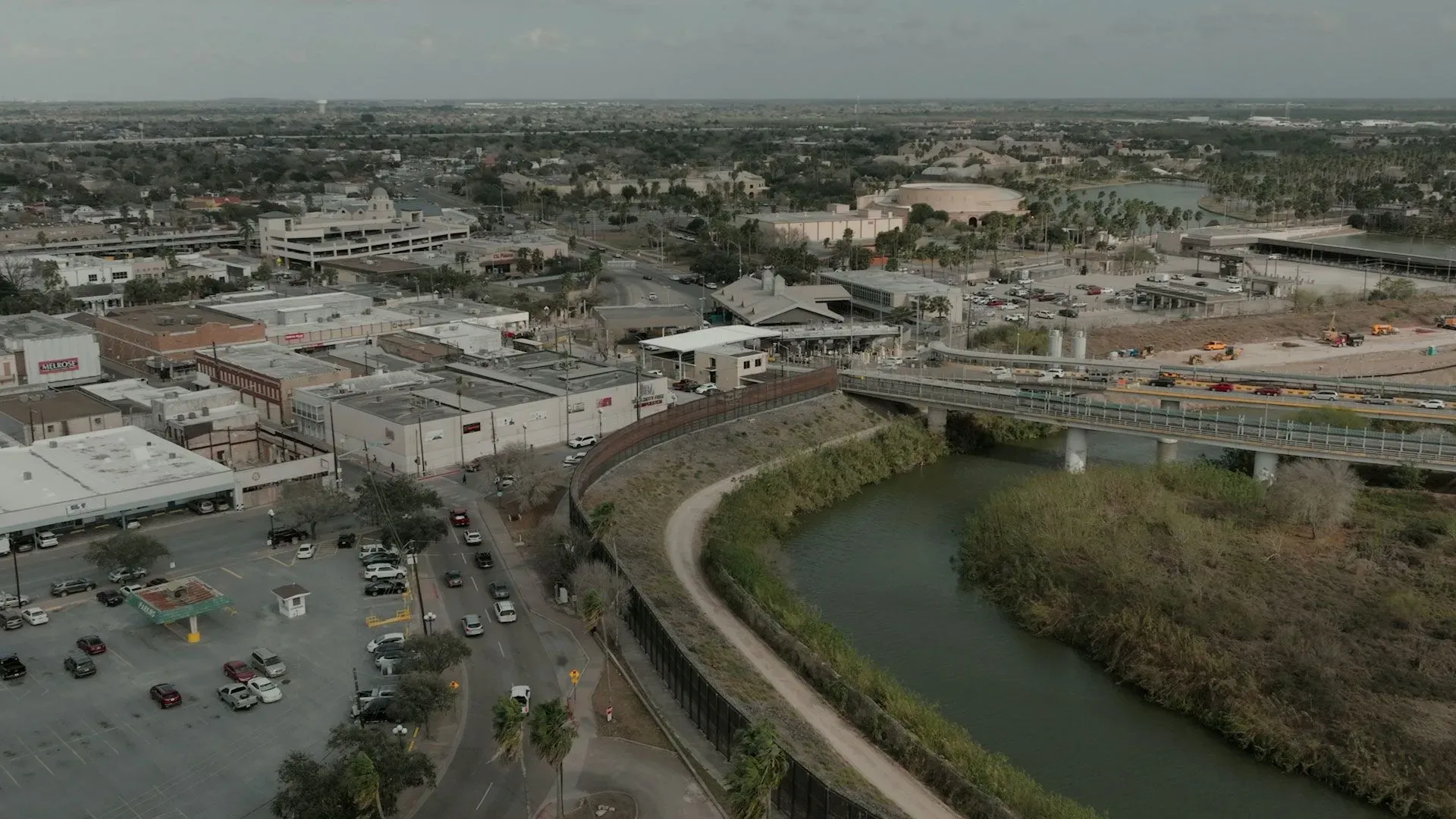 منظر جوي لمدينة براونزفيل، يظهر الحدود مع المكسيك، والمباني التجارية، ونهر ريو غراندي، مع التركيز على القضايا السياسية والاقتصادية.