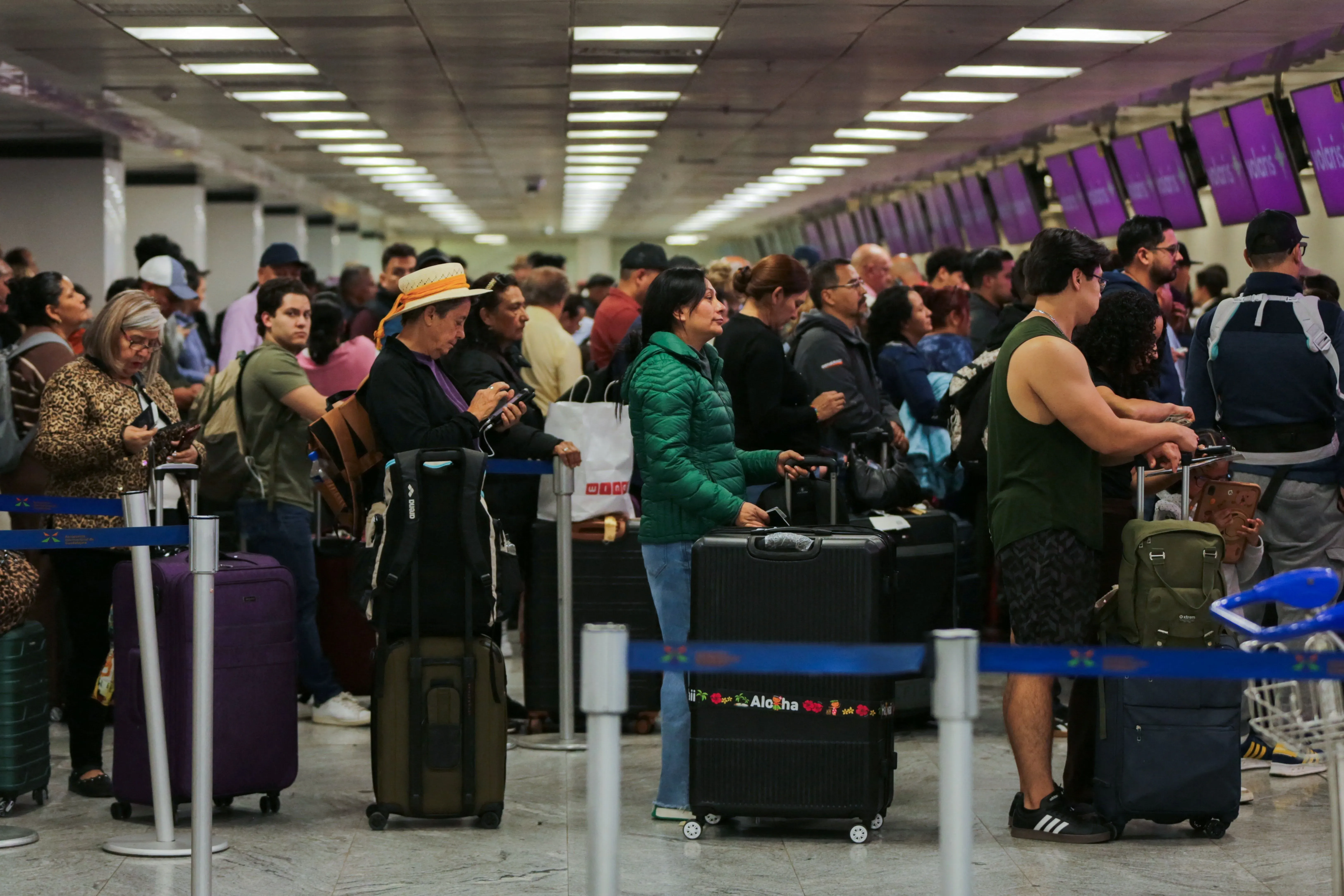 طابور طويل من المسافرين في مطار مزدحم، يحملون حقائبهم بانتظار إنهاء إجراءات السفر، مما يعكس الاضطرابات الناتجة عن الأحداث الأخيرة في المكسيك.