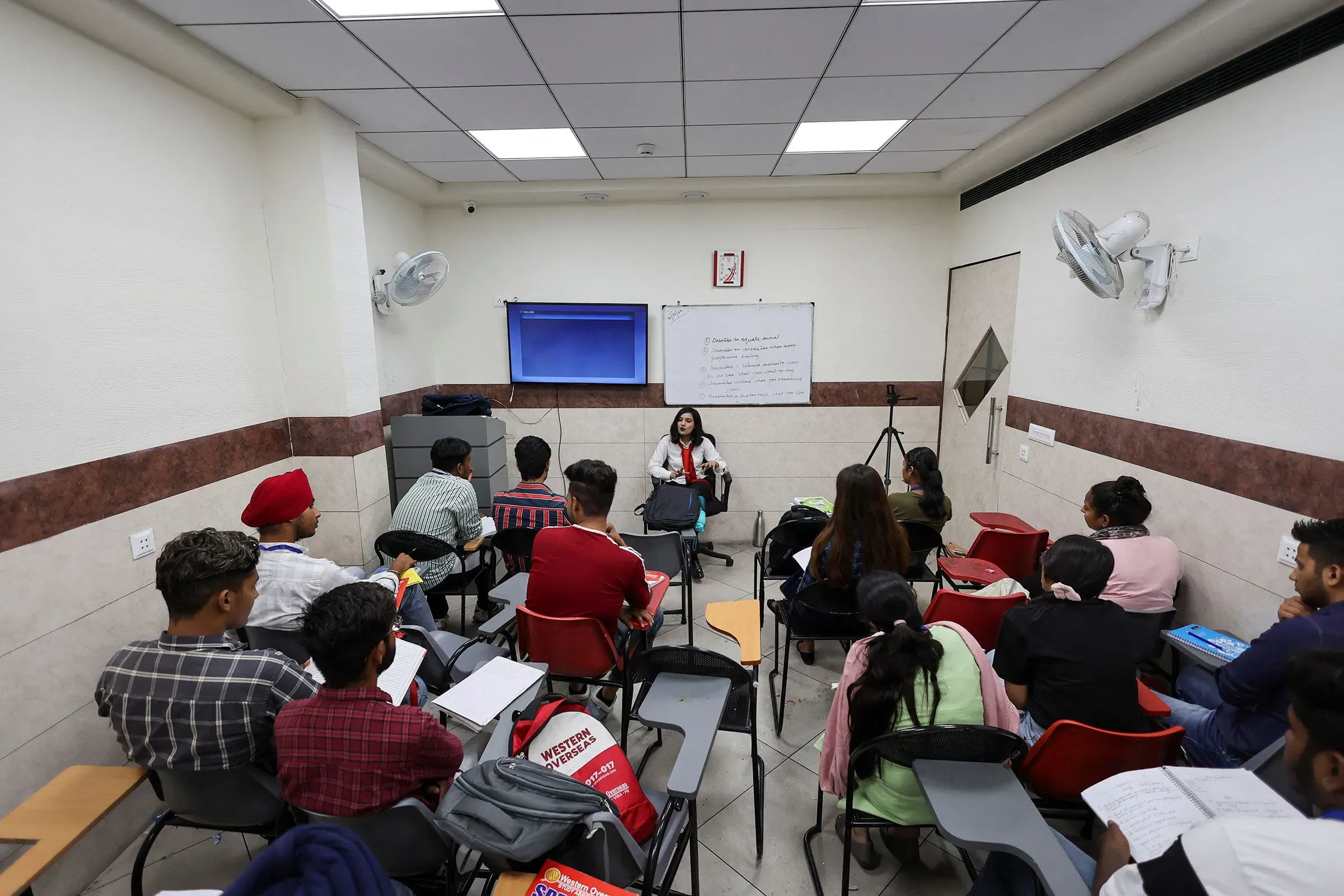 فصل دراسي يتضمن مجموعة من الطلاب يتلقون دروسًا في اللغة الإنجليزية، مع معلمة تتحدث إليهم في بيئة تعليمية حديثة.