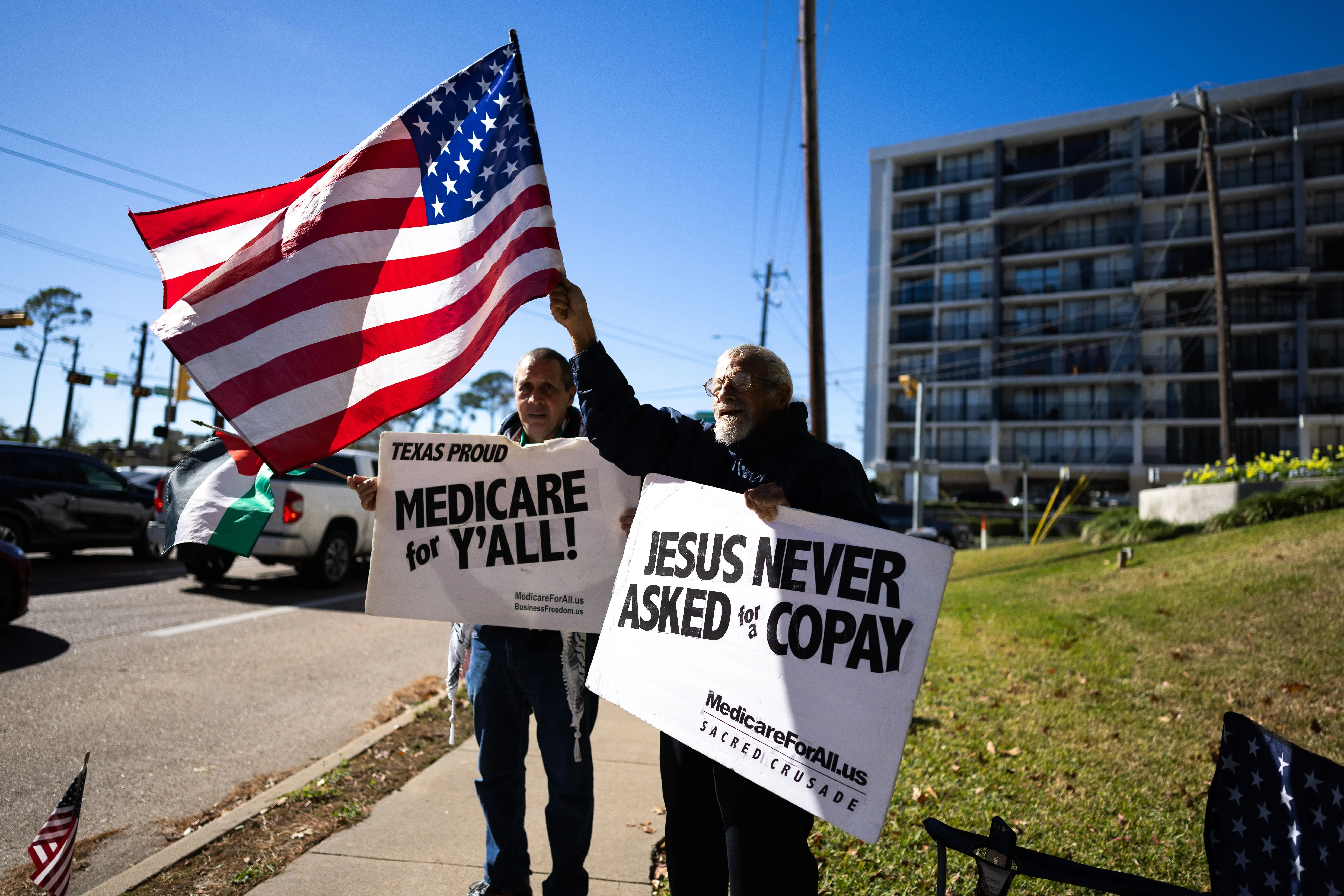 محتجون يحملون لافتات تدعو إلى الرعاية الصحية للجميع، مع علم أمريكي، في تكساس. تعكس الصورة القضايا السياسية والاجتماعية الحالية.