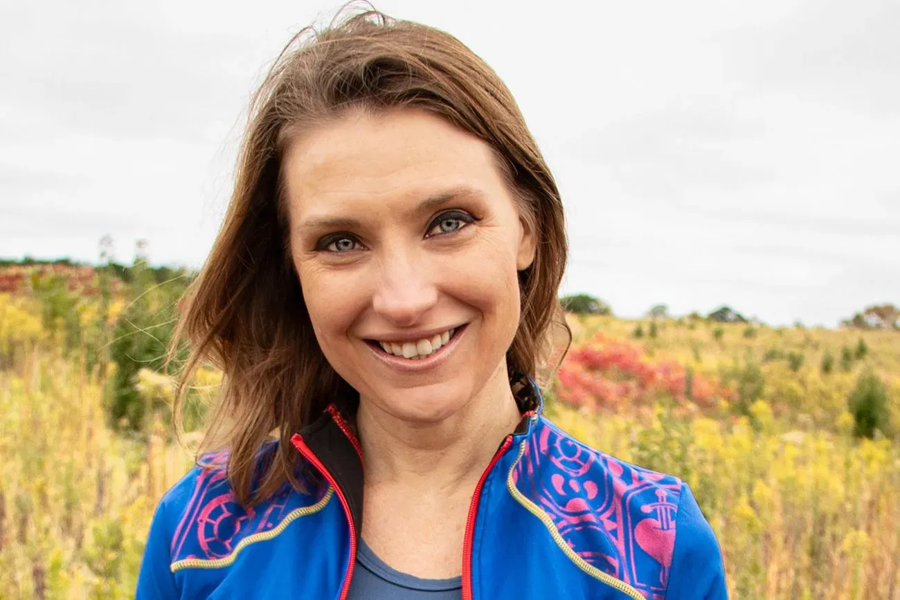 صورة لورين بليس مبتسمة في ملابس رياضية زرقاء، تظهر خلفها طبيعة خضراء، تعكس حيويتها وشغفها بالجري.