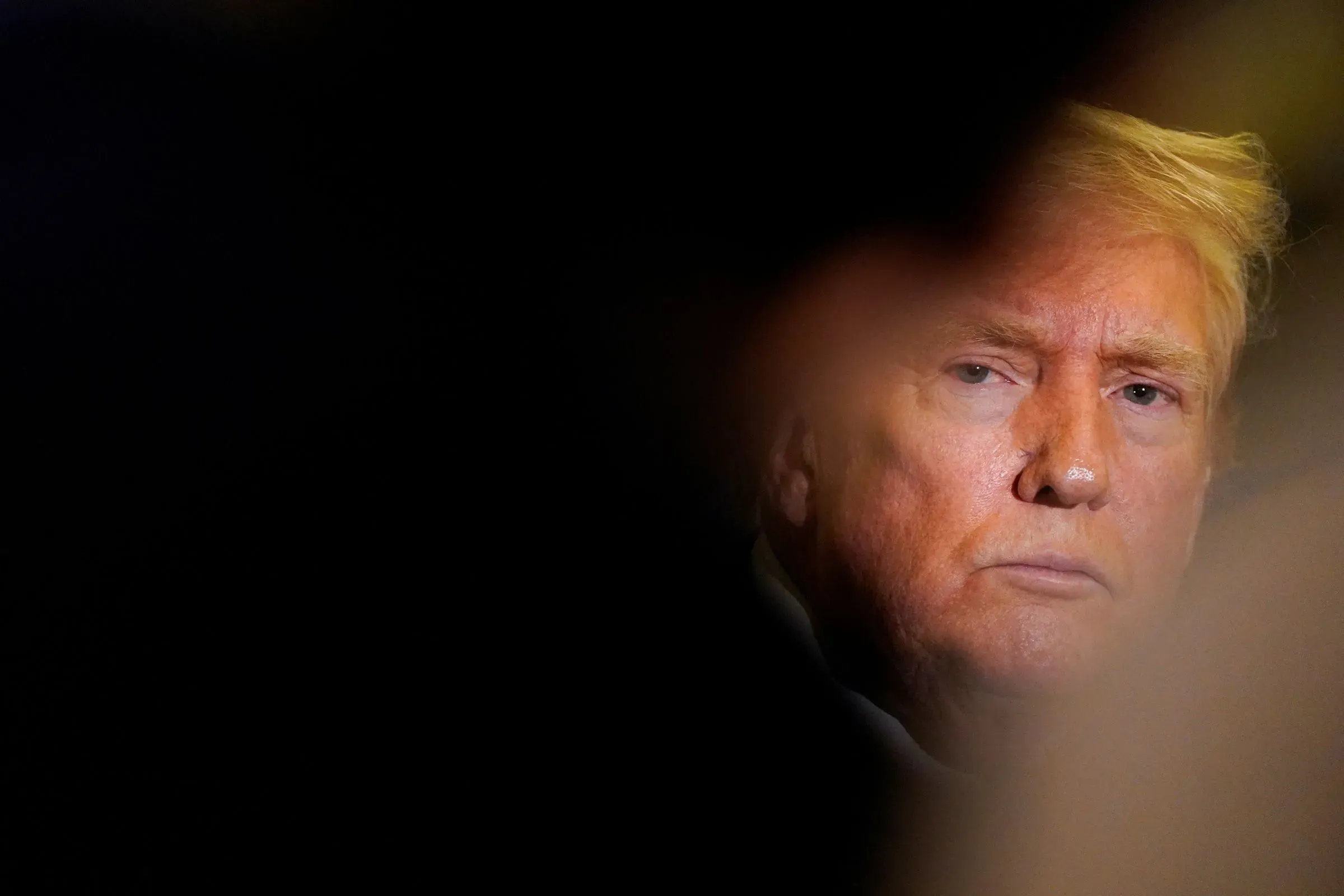 صورة تظهر دونالد ترامب بتعبير جاد، محاطًا بخلفية داكنة، تعكس التوترات المحيطة بفضيحة جيفري إبشتاين وتأثيرها على الشخصيات البارزة.