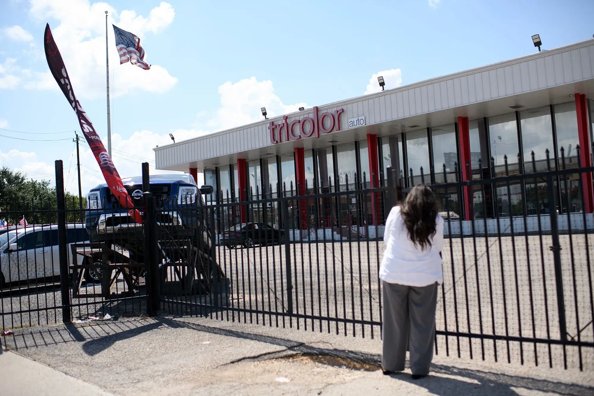 موقع شركة Tricolor لبيع السيارات، حيث تظهر امرأة تنظر من خلف السياج. يعكس المشهد تأثير إفلاس الشركة على المشترين.