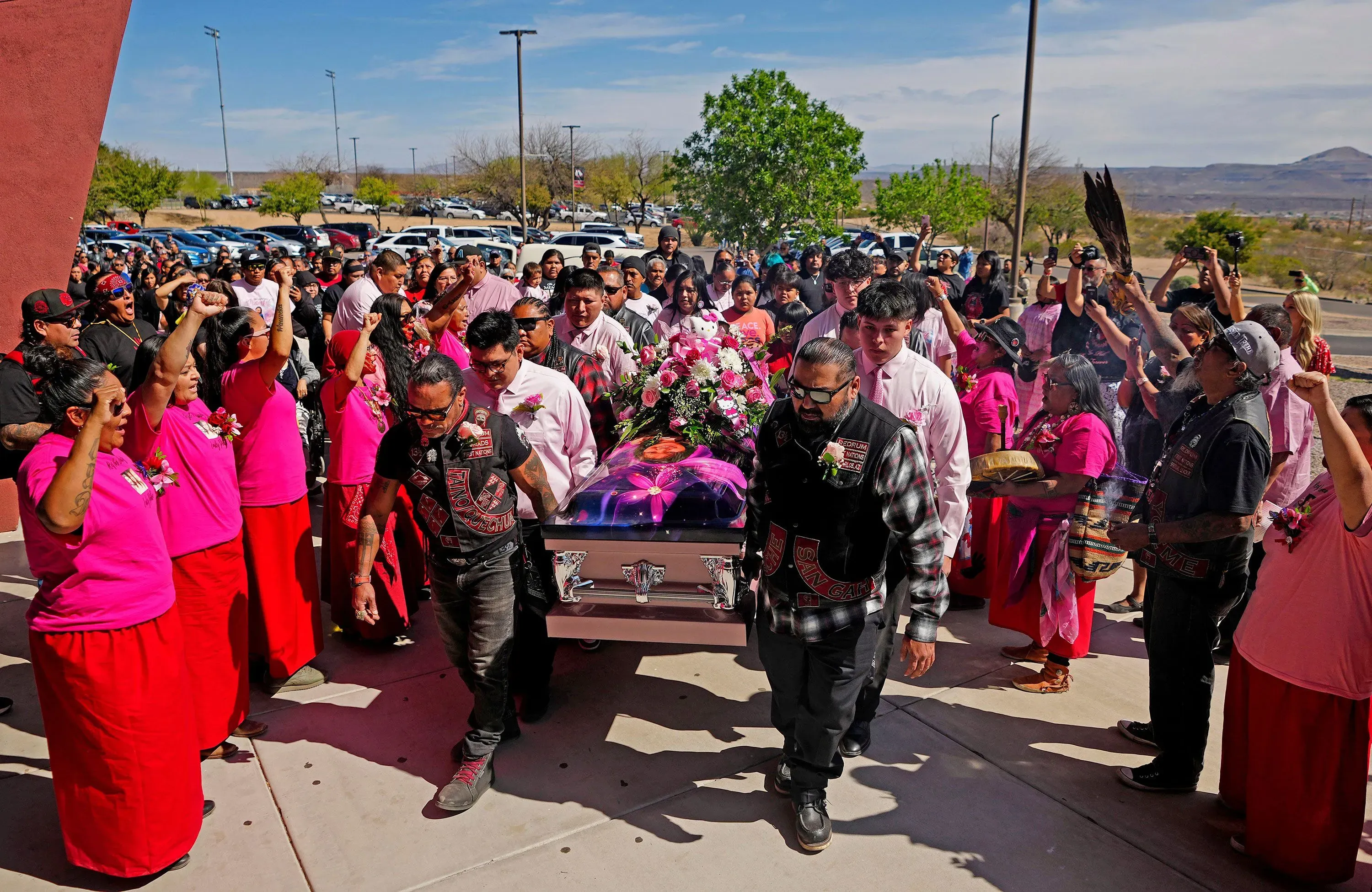 تجمع حشود من أفراد قبيلة سان كارلوس أباتشي في مراسم تأبين إيميلي بايك، حاملين نعشها المزخرف بالورود، معبرين عن الحزن والمطالبة بالعدالة.
