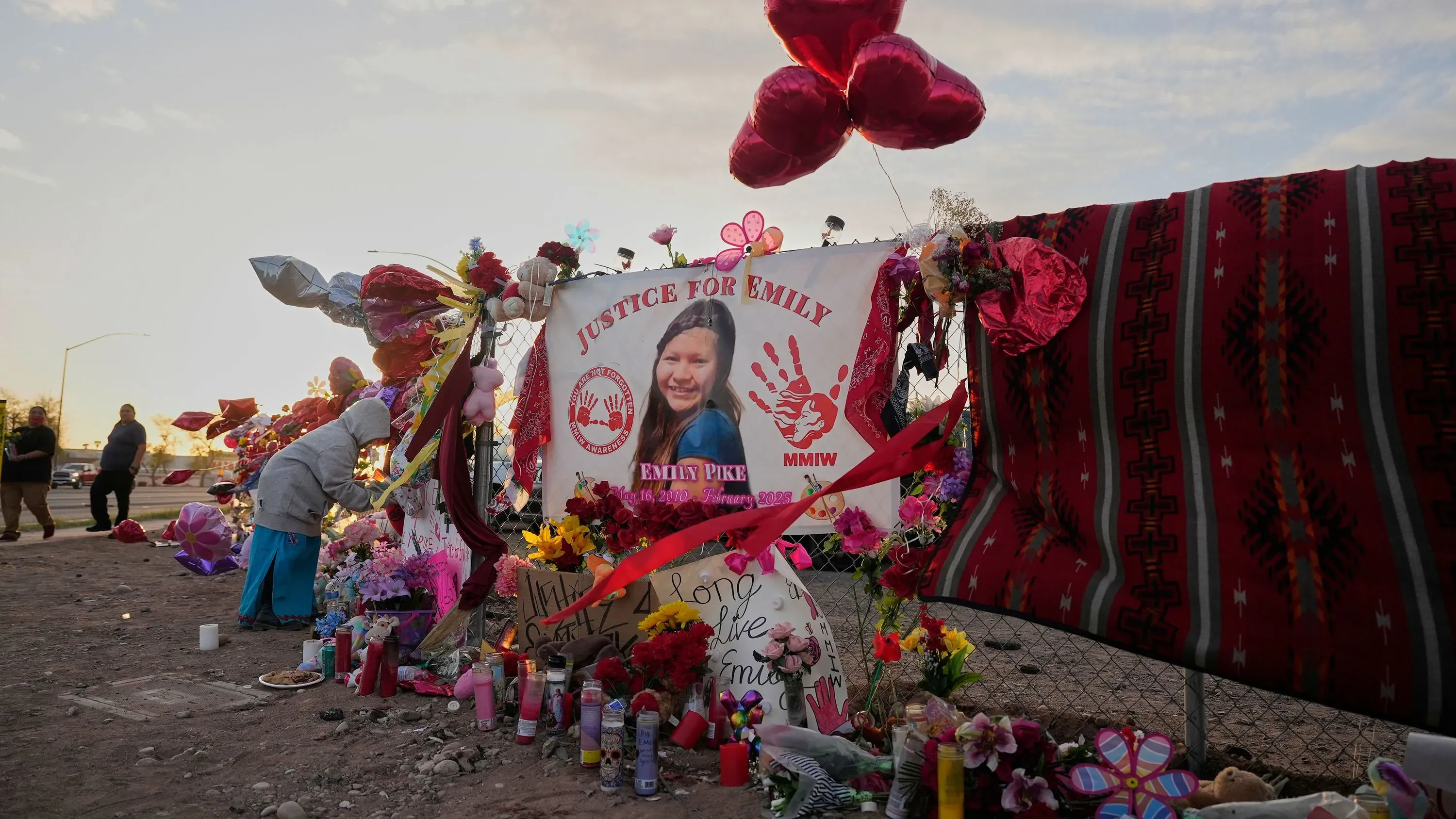 موقع تذكاري لإيميلي بايك، يضم لافتة "العدالة لإيميلي" وزهوراً وبالونات حمراء، يعكس الحزن والأمل في تحقيق العدالة.