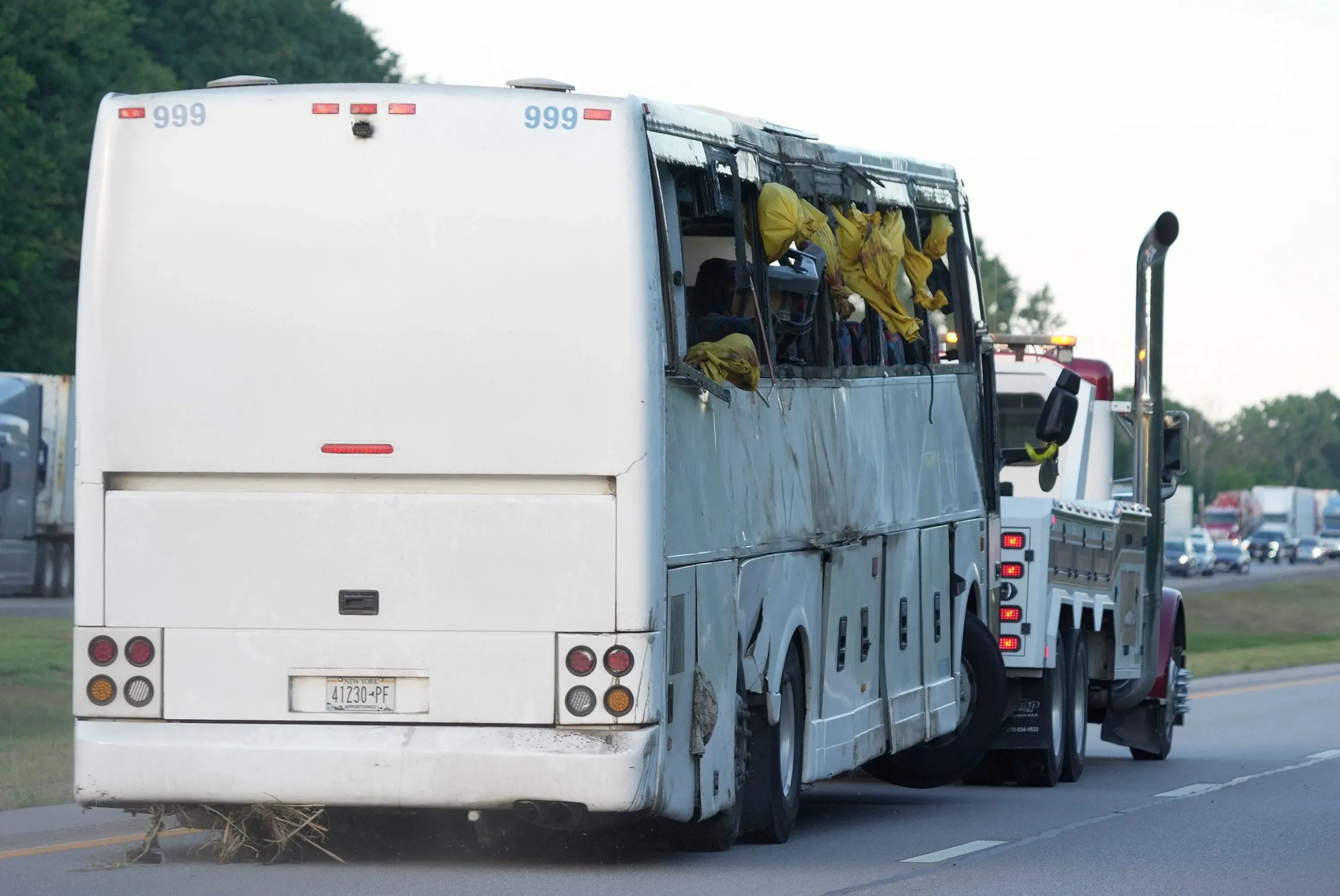 حافلة سياحية متضررة على جانب طريق ولاية نيويورك، مع نوافذ مكسورة وأكياس صفراء، بعد حادث مروع أسفر عن إصابات متعددة.