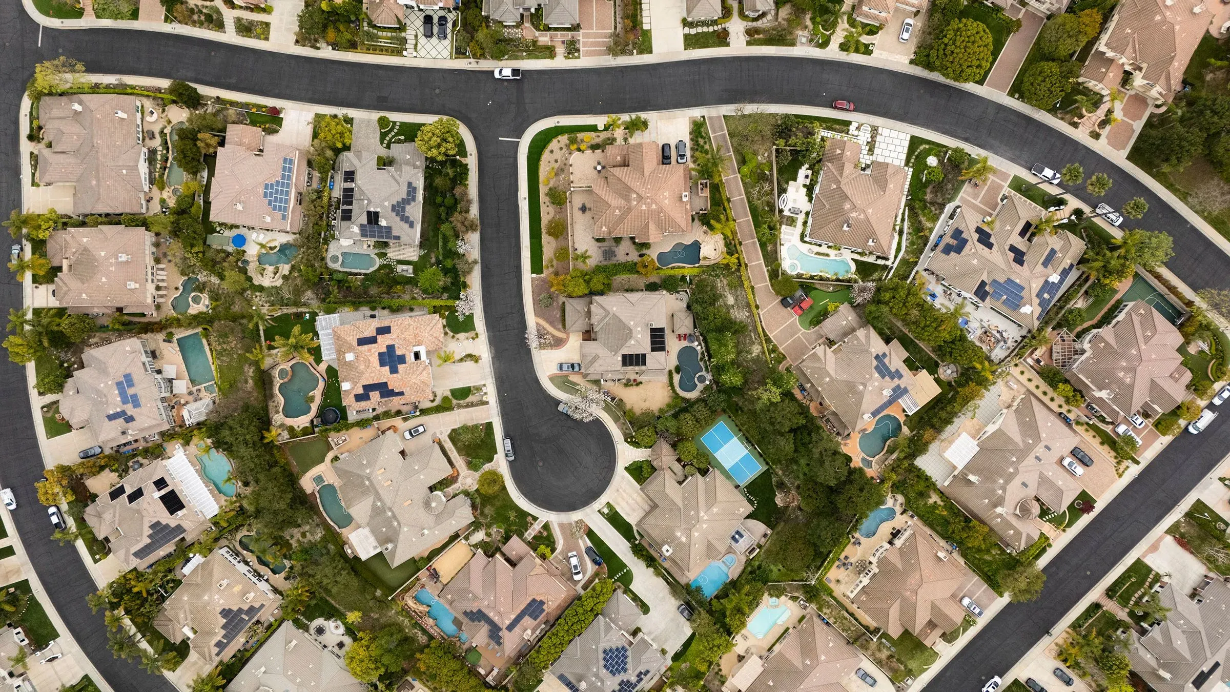 صورة جوية لحي سكني يظهر منازل فاخرة مع مسابح وحدائق، تعكس ارتفاع أسعار العقارات وتأثير الضرائب العقارية.