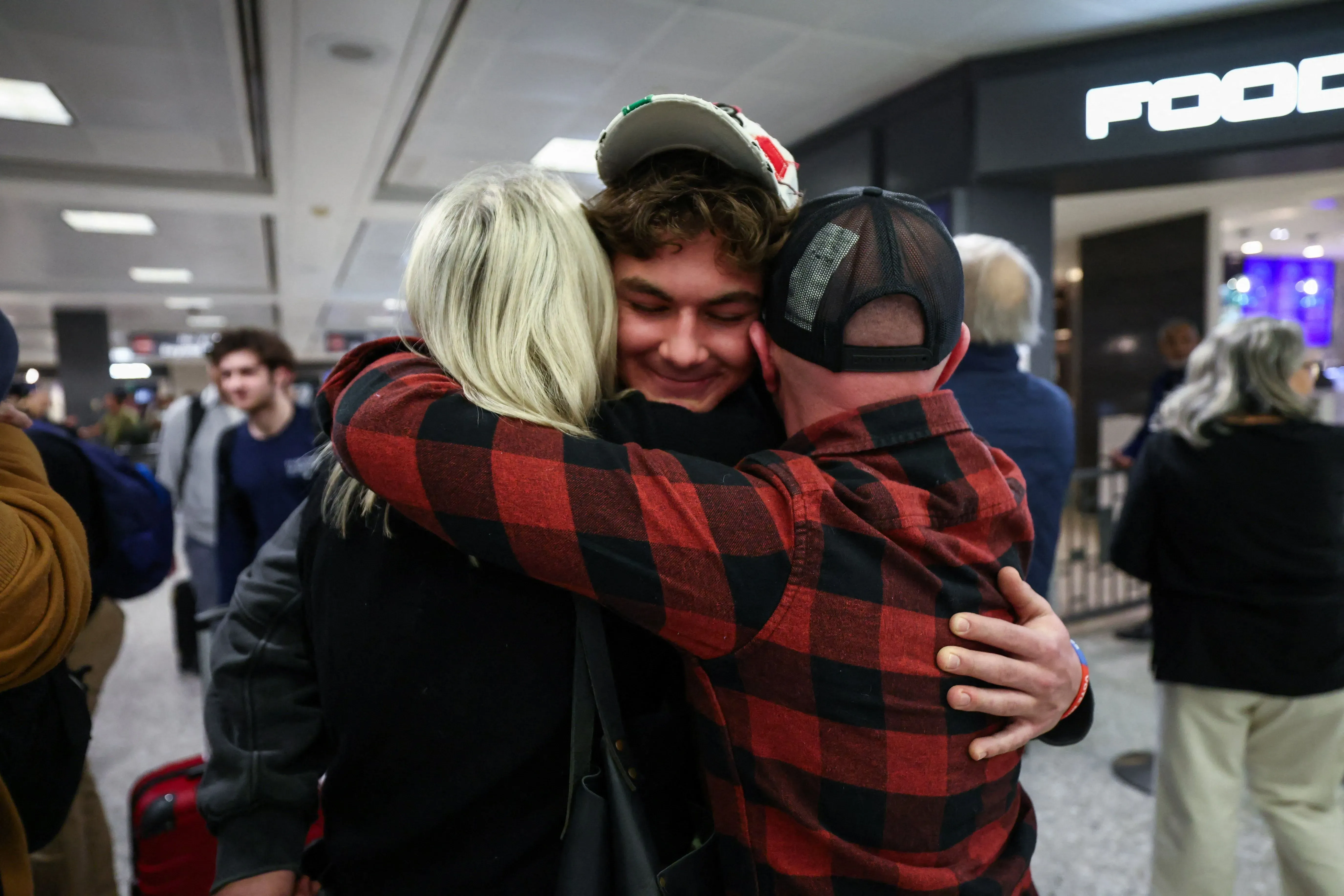 عناق مؤثر بين ثلاثة أشخاص في مطار، يعبر عن الفرح والارتياح بعد لم شملهم وسط الأزمات الحالية في الشرق الأوسط.