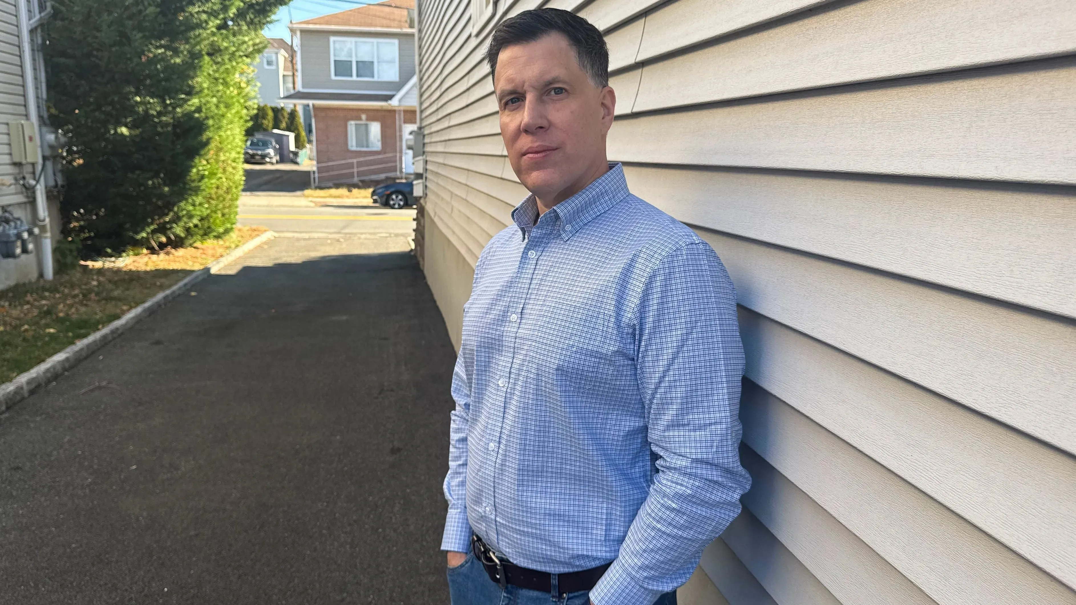 جو نوفاك يقف بجانب جدار منزله، يعكس القلق بعد تعرضه لعملية احتيال عبر الإنترنت تتعلق بالاستثمار في العملات الرقمية.