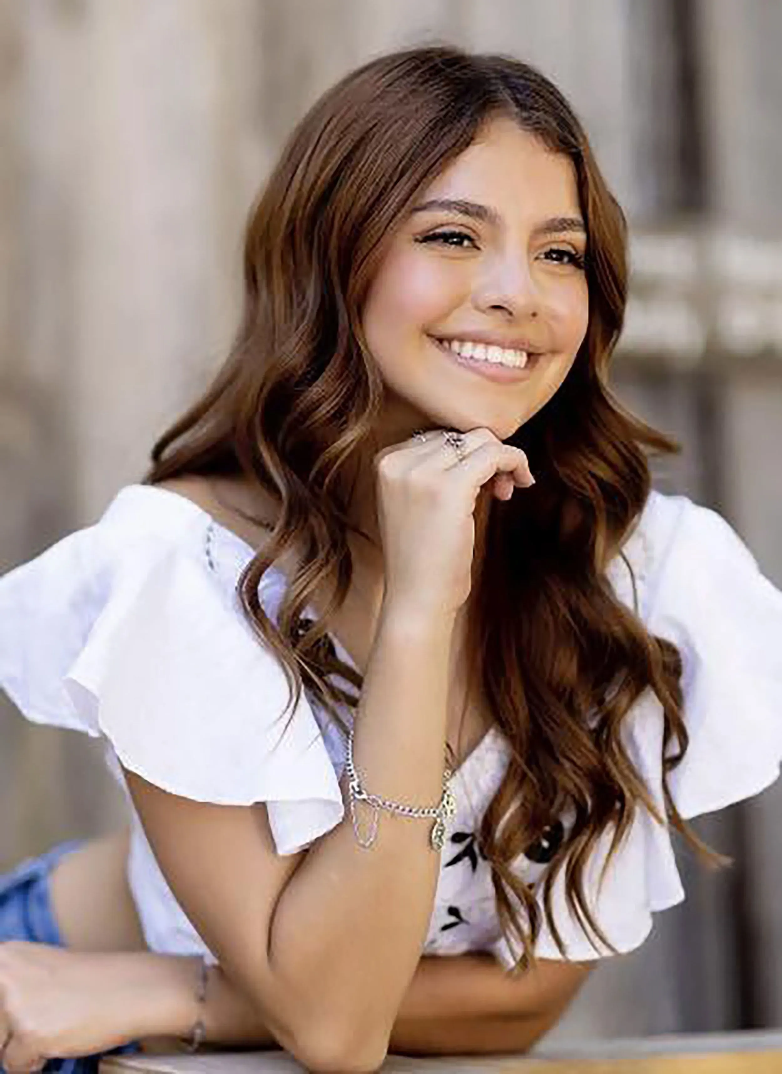 صورة لفتاة شابة مبتسمة تحمل أسلوبًا عصريًا، ترتدي قميصًا أبيض مزخرفًا، تعكس الأمل وسط حالة من القلق بعد اختفائها.