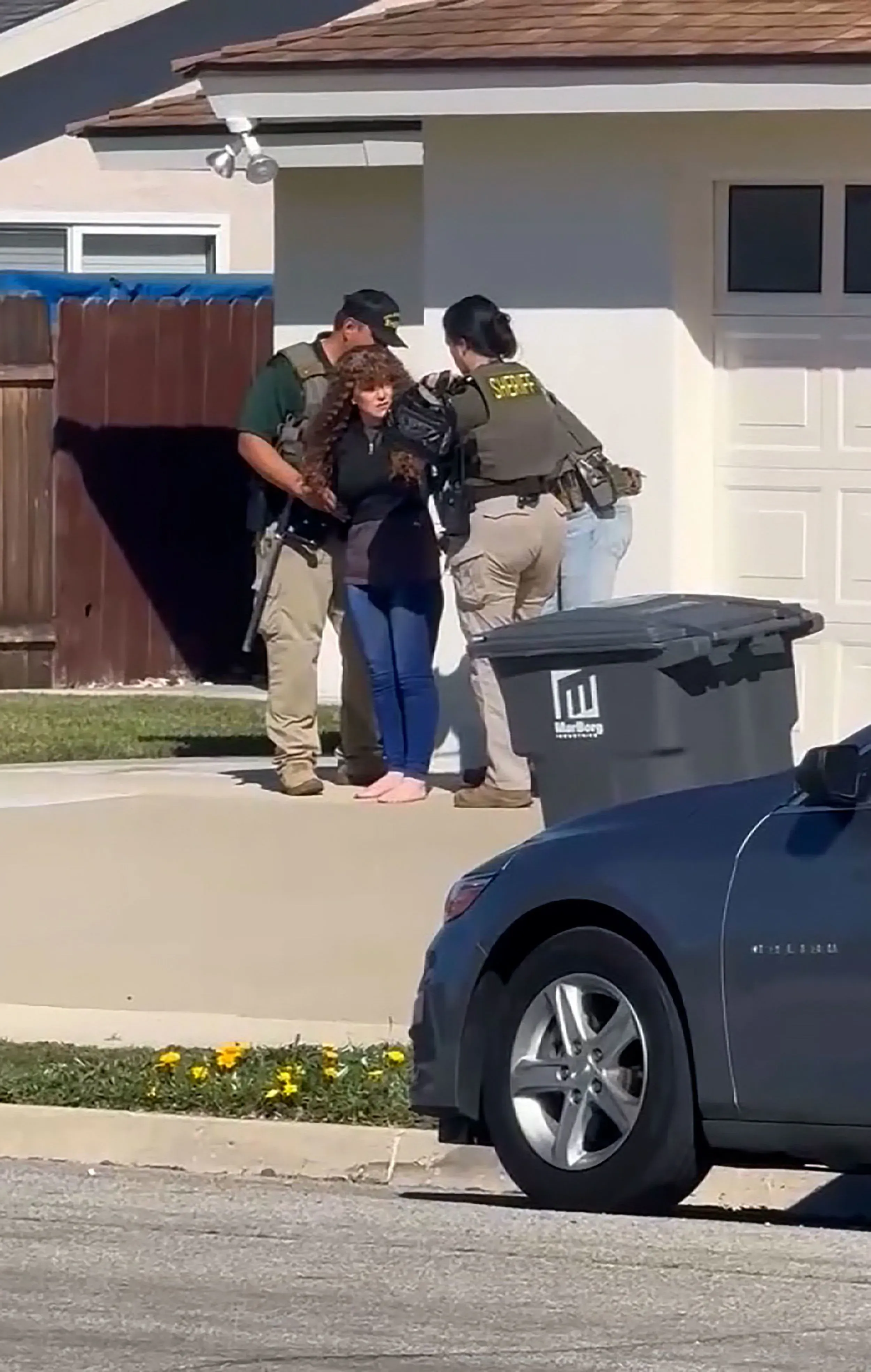 اعتقال آشلي بازارد، والدة ميلودي، من قبل رجال الشرطة، مع وجود سيارة شيفروليه ماليبو في الخلفية، أثناء التحقيق في اختفاء ابنتها.