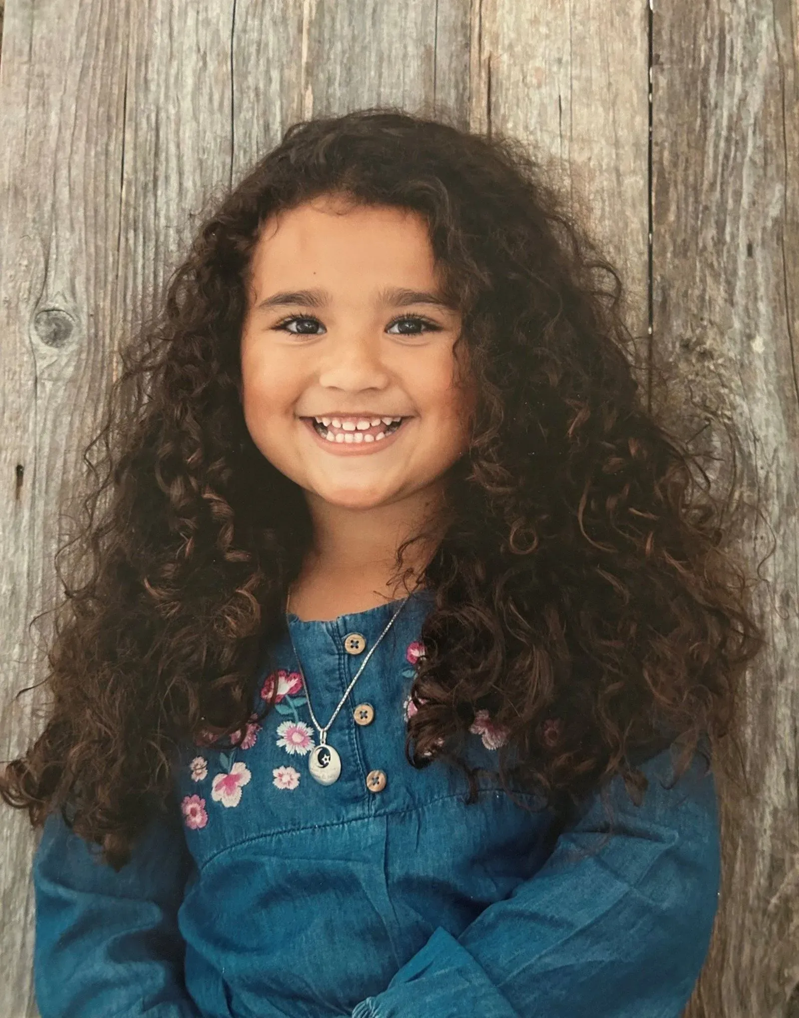 صورة لطفلة صغيرة ذات شعر بني مجعد، ترتدي قميصاً أزرق مزين بالزهور، مبتسمة أمام خلفية خشبية. تعود الصورة لعام 2023، وتظهر في سياق البحث عن ميلودي بازارد.