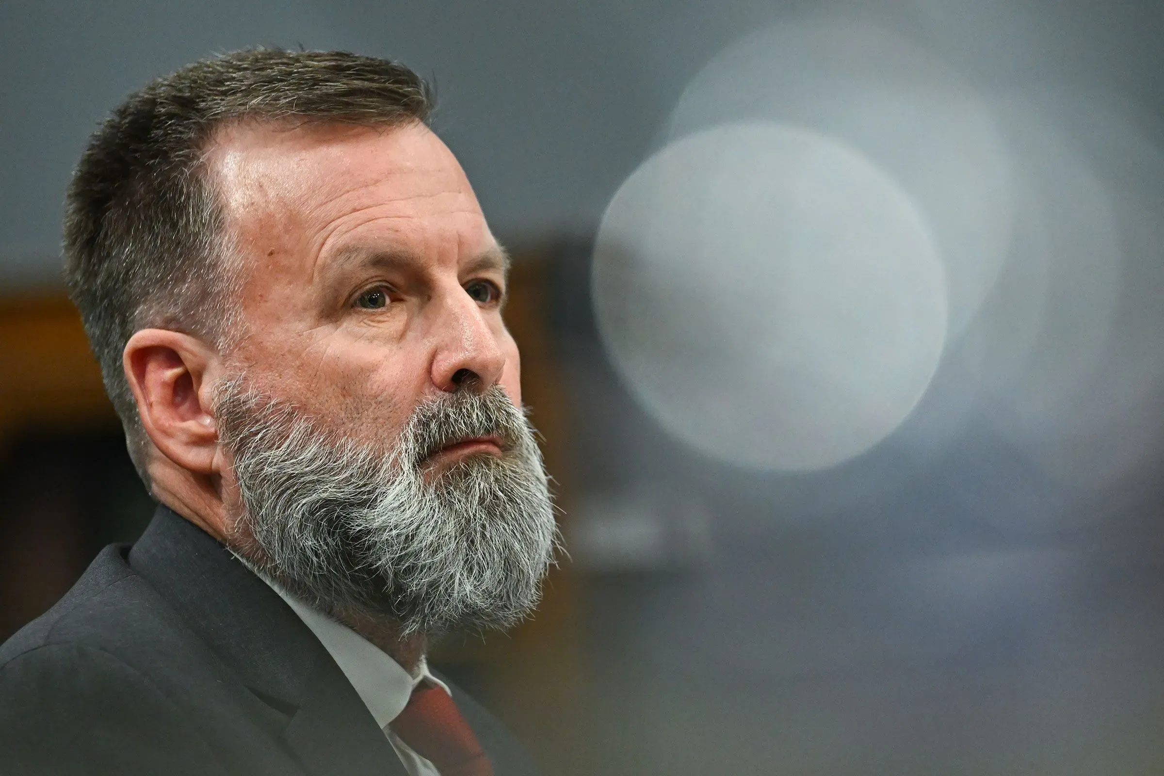 جريج فيليبس، مسؤول في إدارة الطوارئ الفيدرالية، يظهر أثناء جلسة استماع، مع تعبير جاد، وسط أضواء غير واضحة.