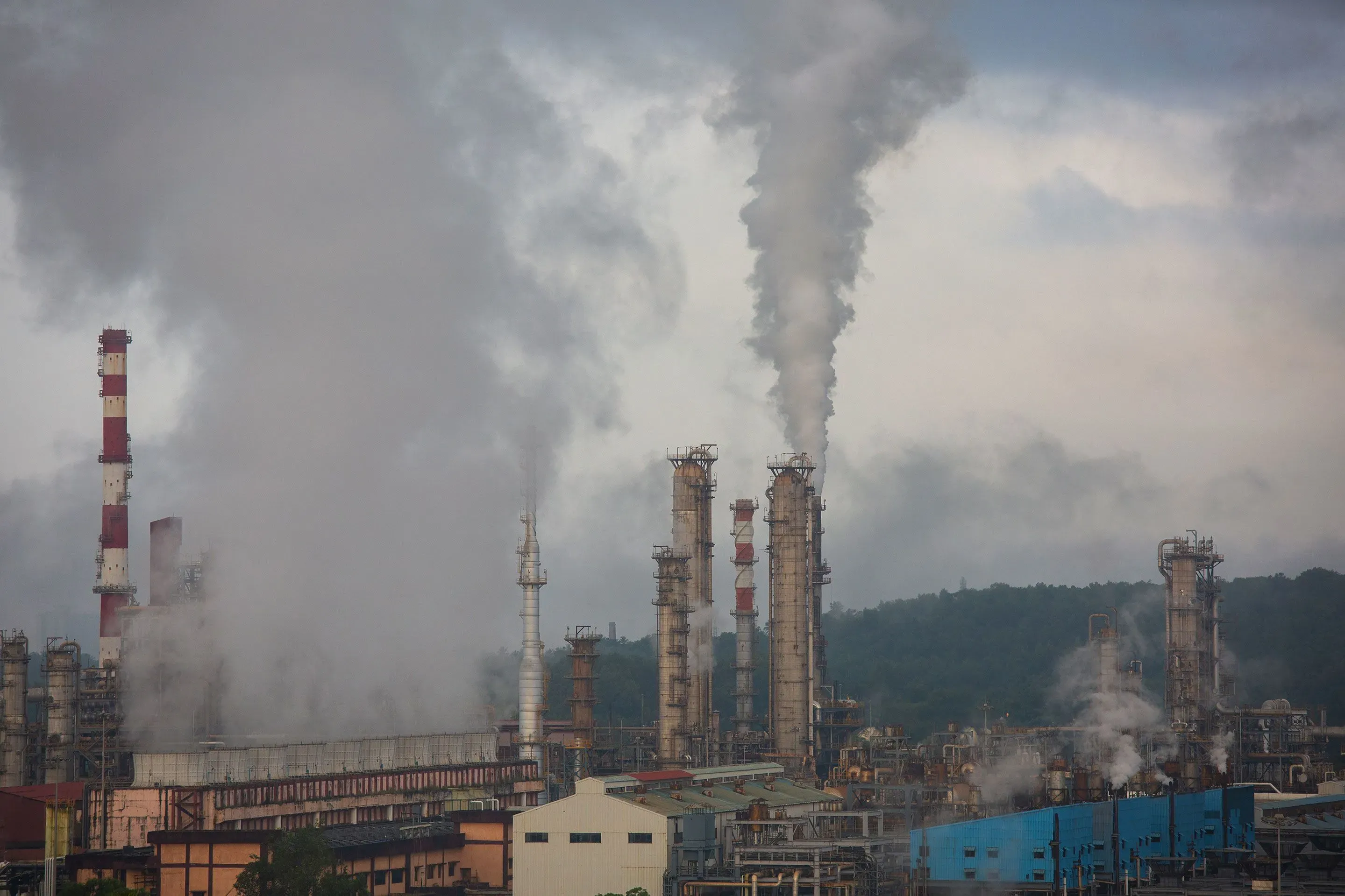 مصنع ضخم يُصدر دخانًا كثيفًا في سماء نيودلهي، مع وجود مداخن بارزة، مما يعكس النشاط الصناعي في المنطقة.