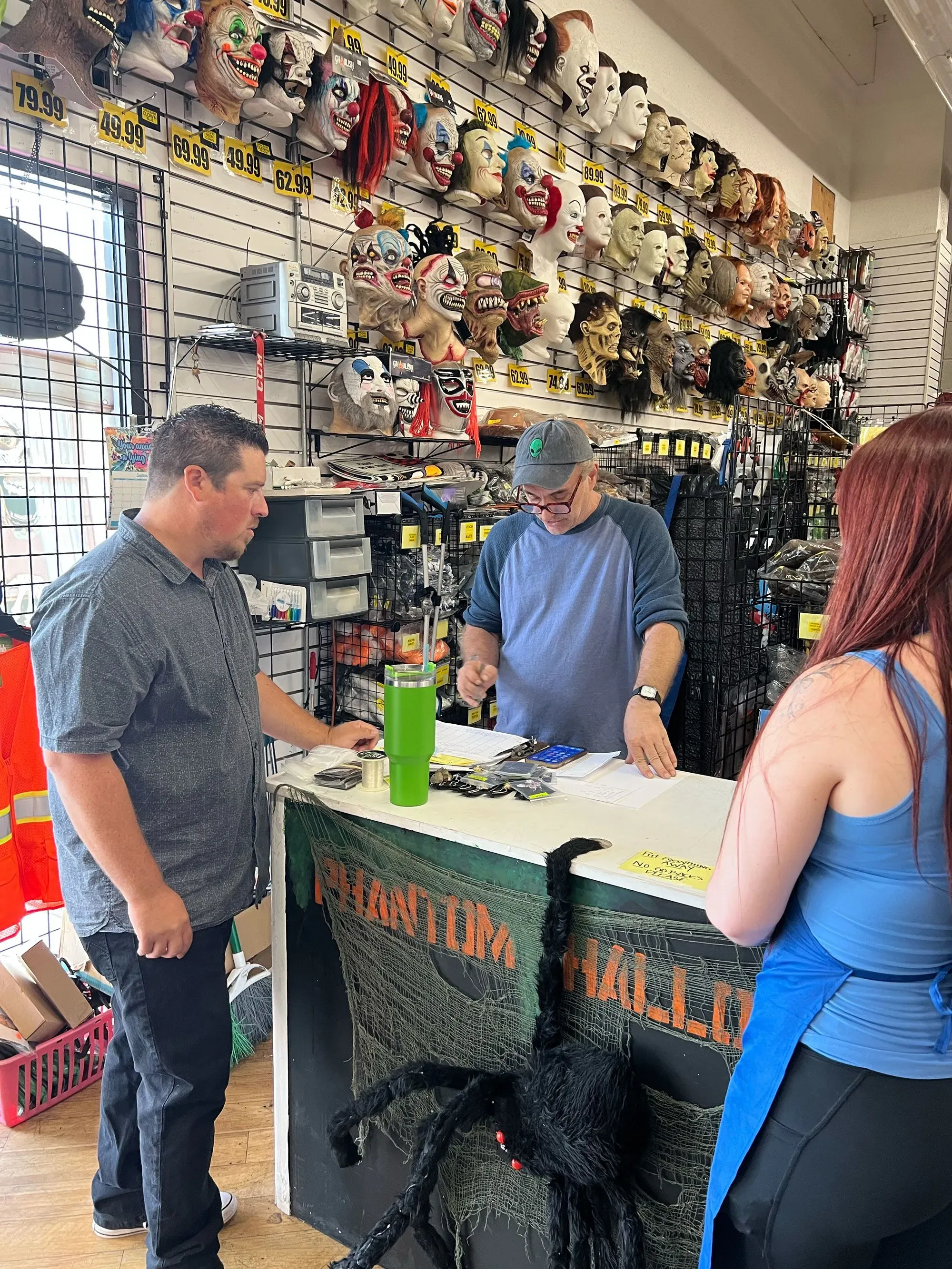 متجر فانتوم هالوين في كاليفورنيا، حيث يتحدث زبون مع موظف حول أسعار الأزياء التنكرية، مع عرض أقنعة مرعبة على الحائط.