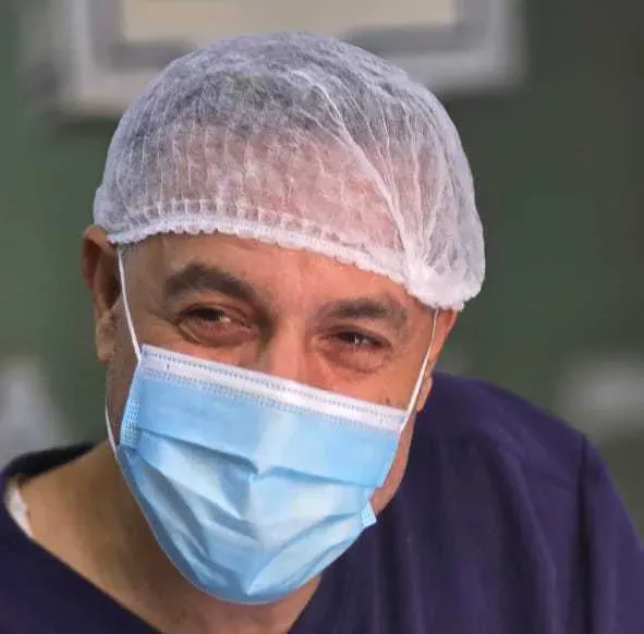دكتور حسام أبو صفية مبتسم، يرتدي قبعة طبية وقناع وجه، في مستشفى كمال عدوان ببيت لاهيا، قبل اعتقاله.