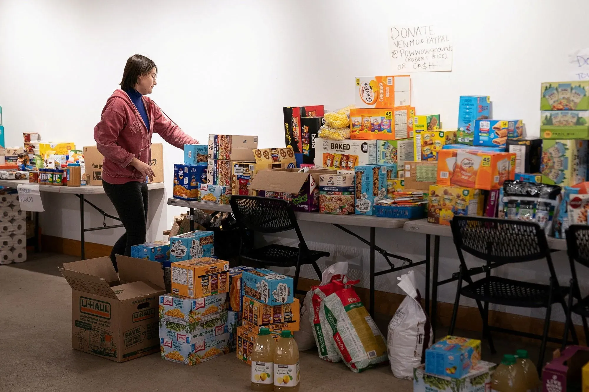 امرأة ترتب صناديق من المواد الغذائية في مركز مجتمعي، حيث تُظهر جهود الدعم للعائلات المتأثرة بعمليات الهجرة في مينيابوليس.