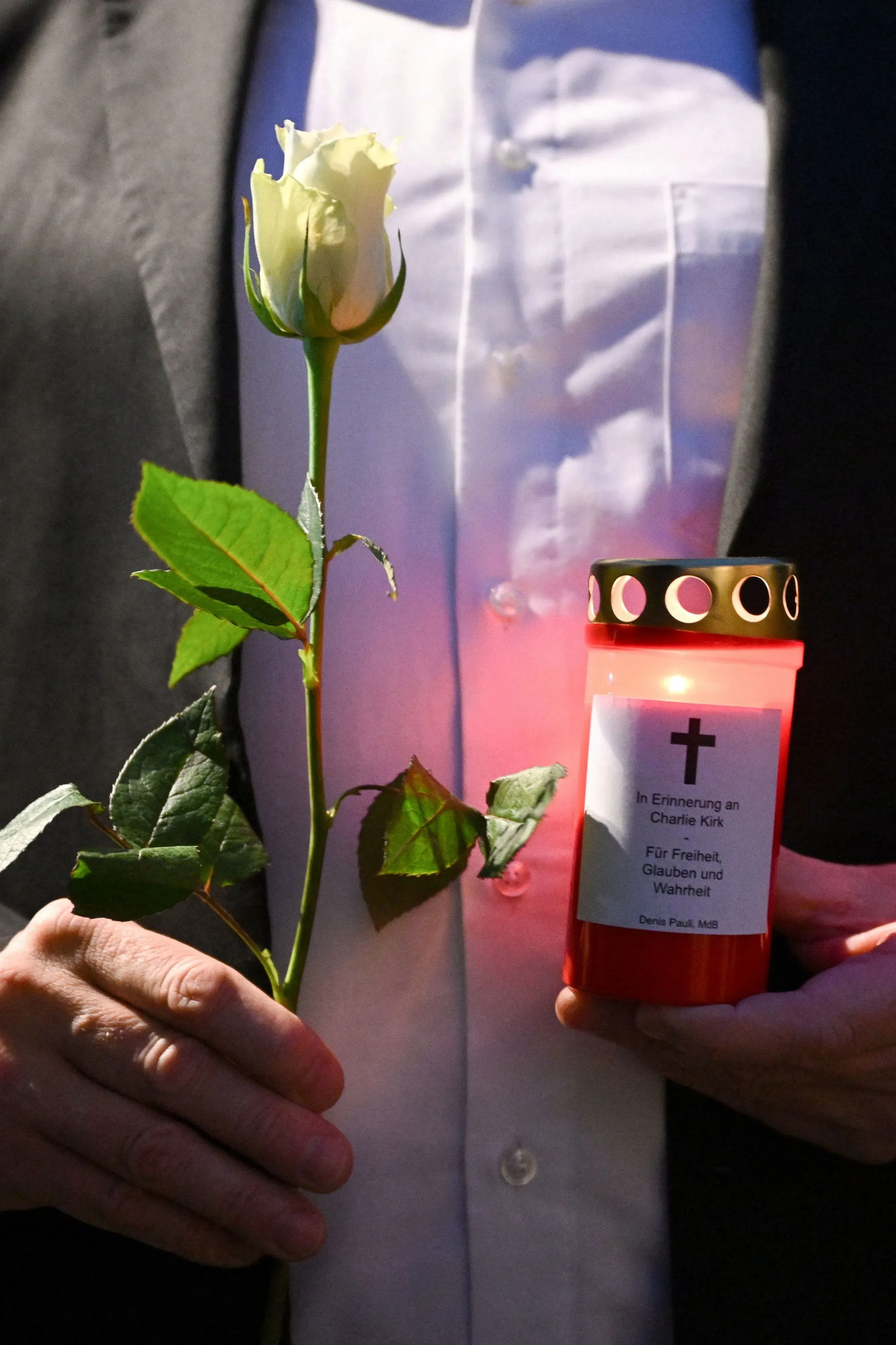 تجمع لتكريم تشارلي كيرك، حيث يحمل شخص وردة بيضاء ووعاء شمعة مضاءة، مع رسالة تعبر عن الحرية والإيمان.