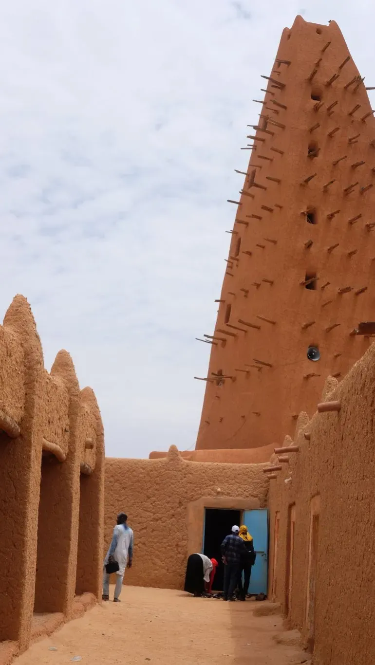 مئذنة المسجد الكبير في أغاديز، بنيت من الطوب الطيني، تبرز فوق المباني المحيطة، بينما يتجول الزوار في المكان.