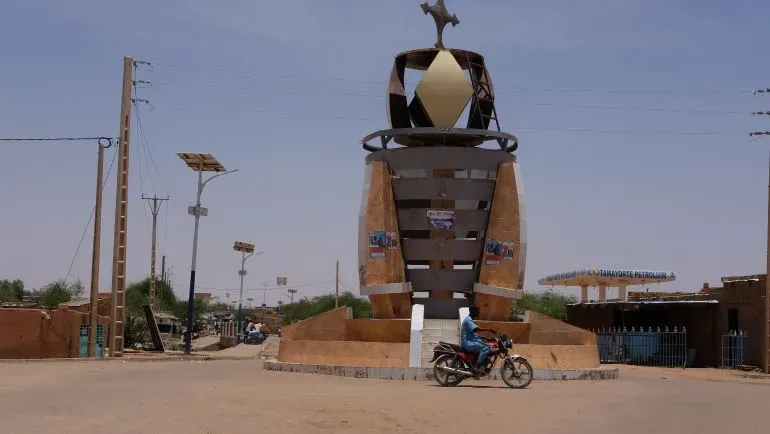 نصب تذكاري في أغاديز، النيجر، يظهر تصميمه الفريد مع دراجة نارية تمر بجواره في يوم مشمس.