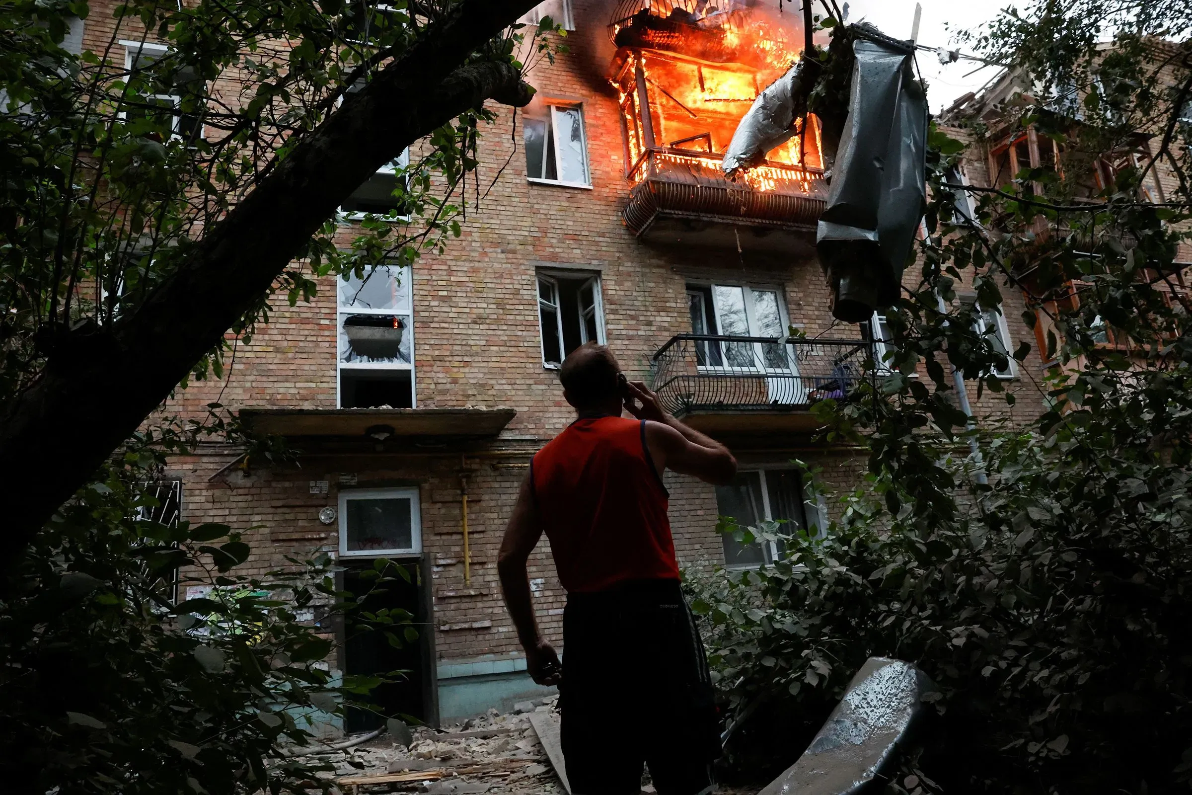 شخص يقف أمام مبنى سكني محترق، حيث تتصاعد النيران من شرفة الطابق العلوي، مما يعكس آثار النزاع في أوكرانيا.