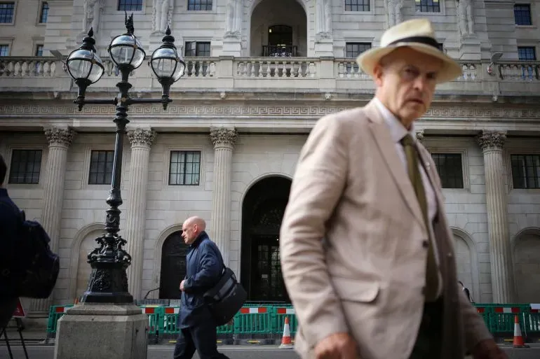 رجلان يسيران بالقرب من مبنى حكومي في لندن، مع تركيز على التوترات المحيطة بالضرائب وتأثيرها على الأثرياء.