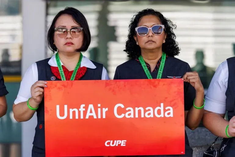مضيفتان جويتان من شركة الخطوط الجوية الكندية تحملان لافتة مكتوب عليها "UnfAir Canada" خلال احتجاج على الأجور وظروف العمل.