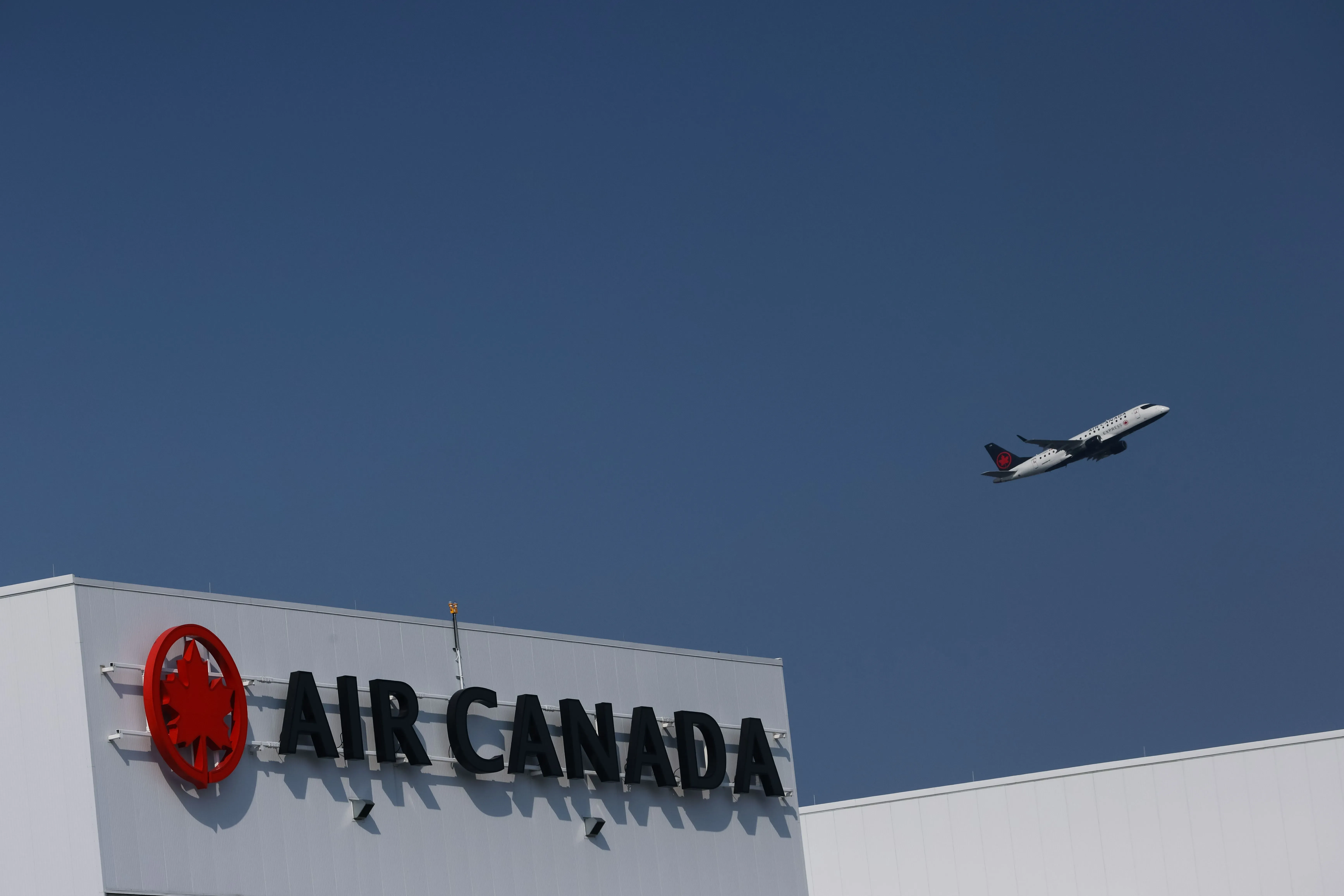 طائرة تابعة للخطوط الجوية الكندية تحلق فوق مبنى يحمل شعار الشركة، في ظل توترات إضراب محتملة تؤثر على السفر.