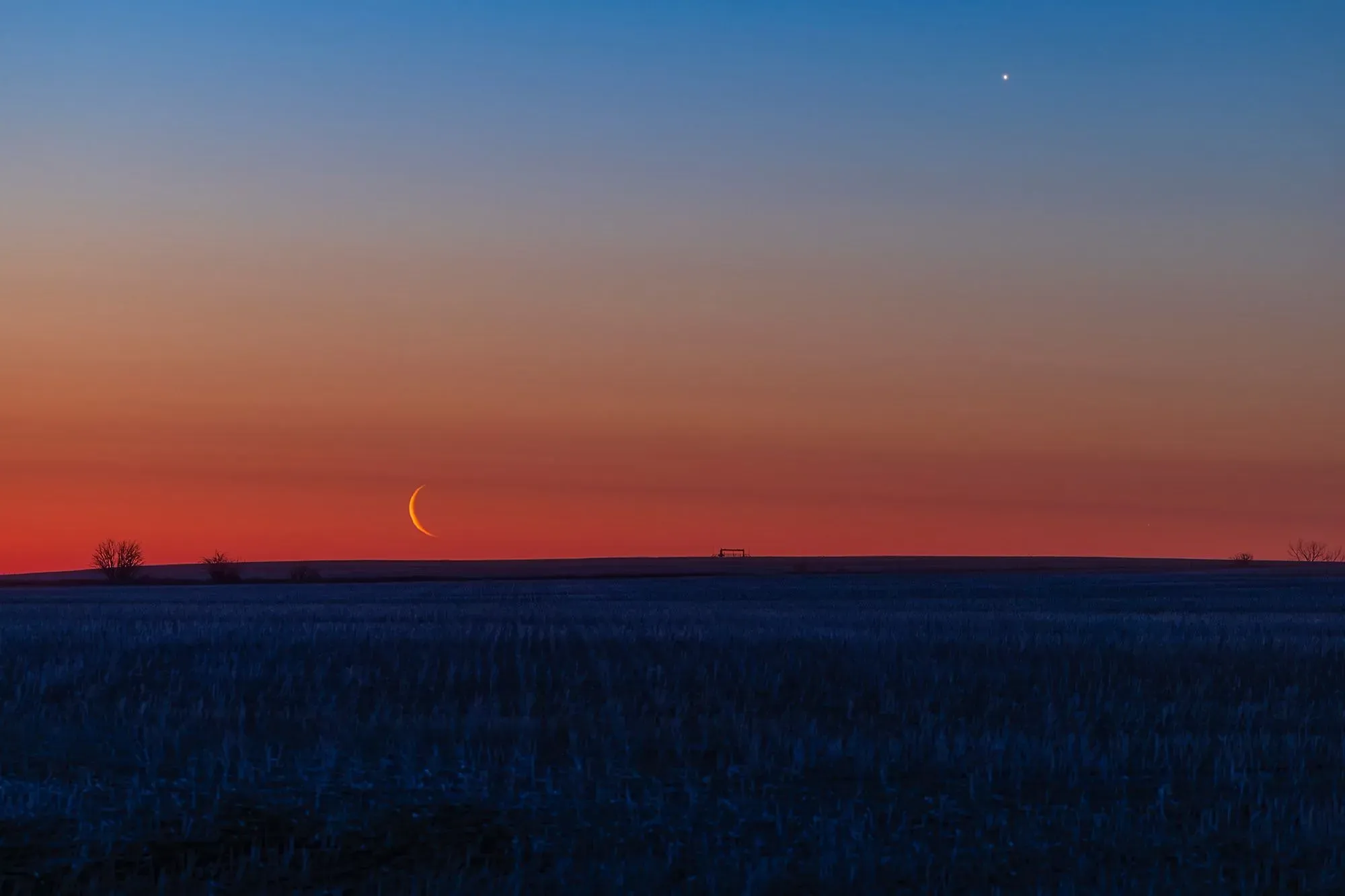 غروب شمس ساحر يظهر فيه قمر هلالي رقيق فوق الأفق، مع كوكب لامع في السماء، مما يبرز جمال السماء في عام 2026.