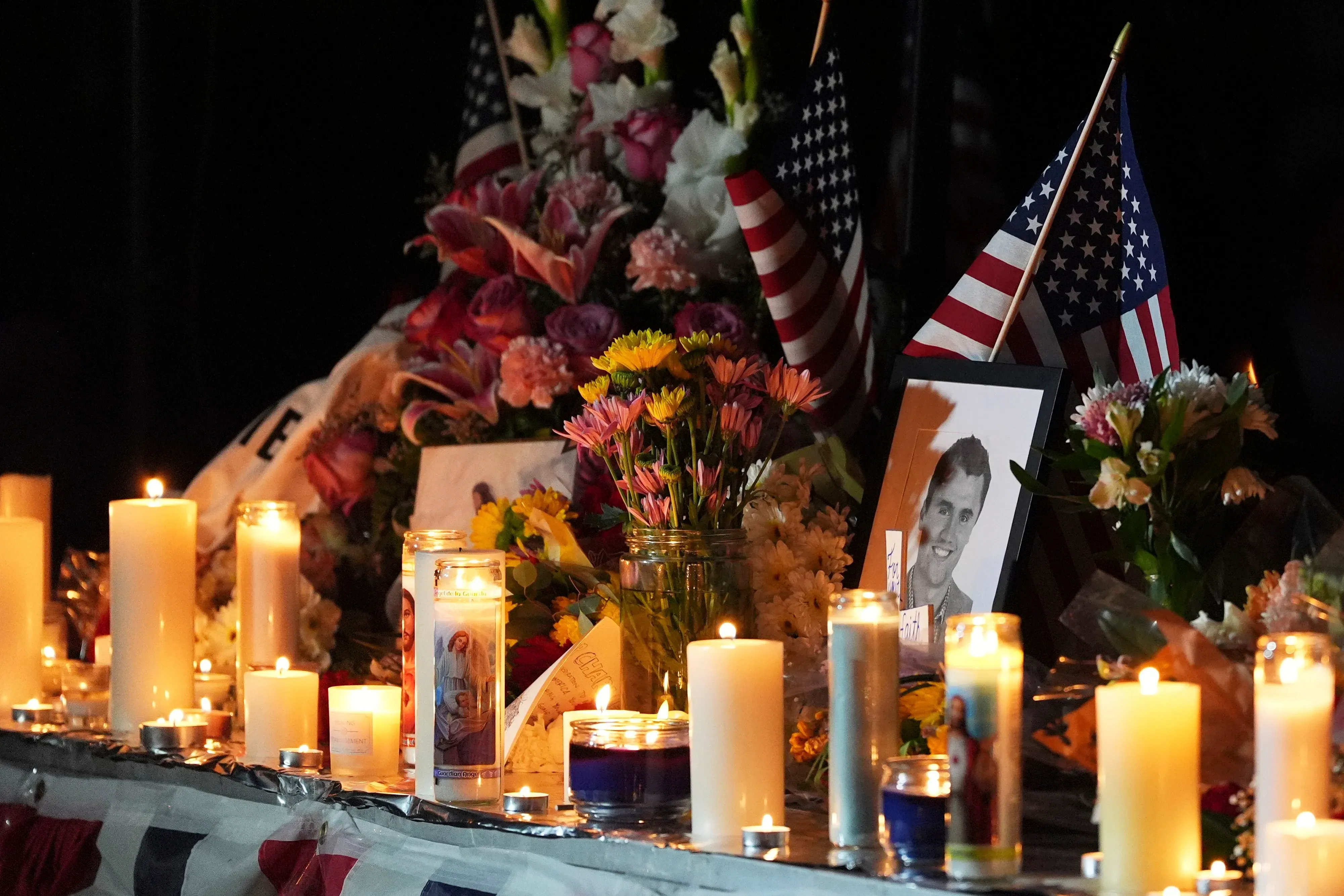 مزار تذكاري مضاء بالشموع مع صورة لتشارلي كيرك، محاط بأعلام أمريكية وزهور، يرمز إلى الحزن والقلق بعد اغتياله.