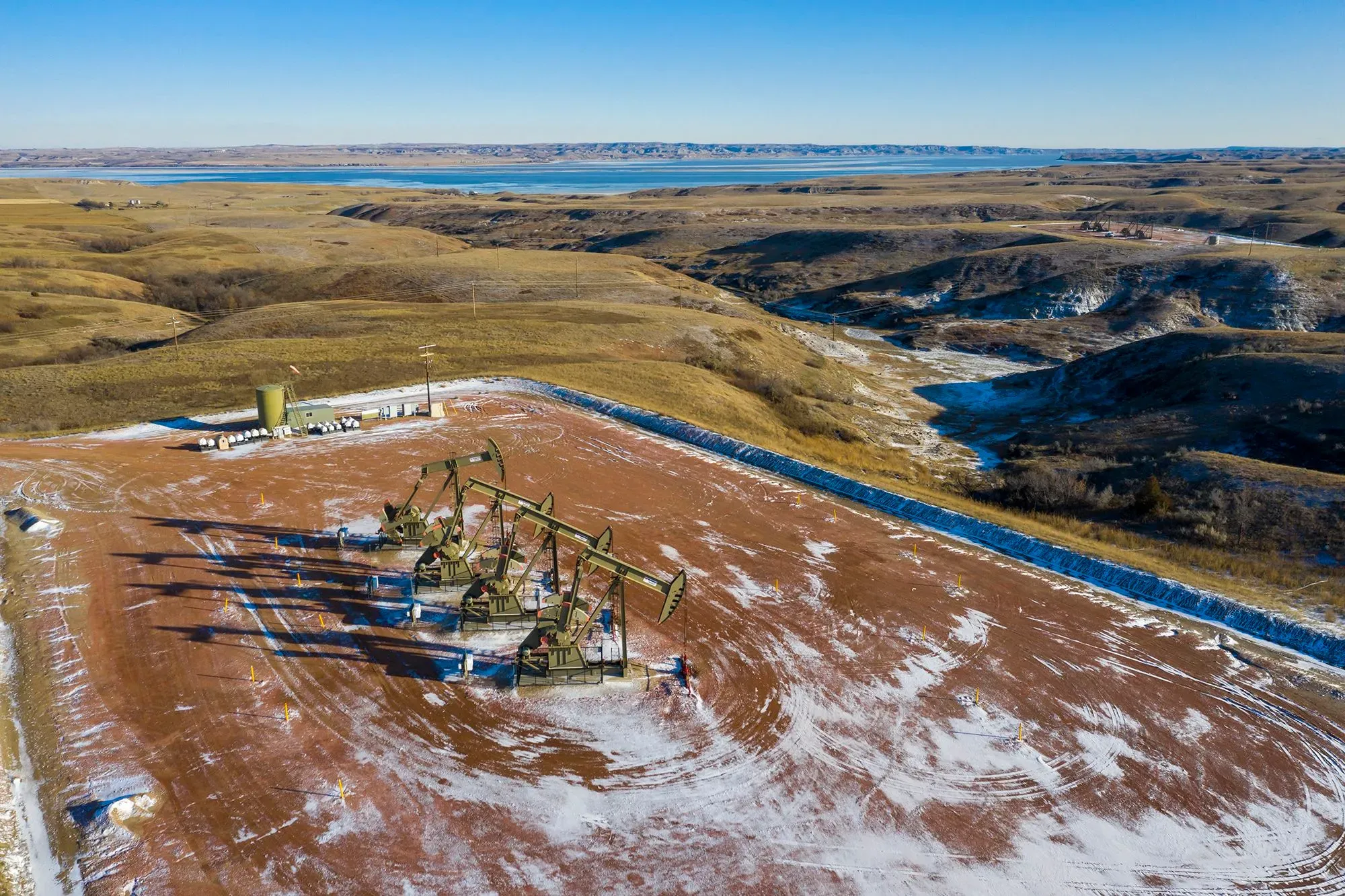 منطقة إنتاج النفط في الولايات المتحدة تظهر مضخات النفط تعمل في حقل مفتوح، مع مناظر طبيعية خضراء وجبال في الخلفية.