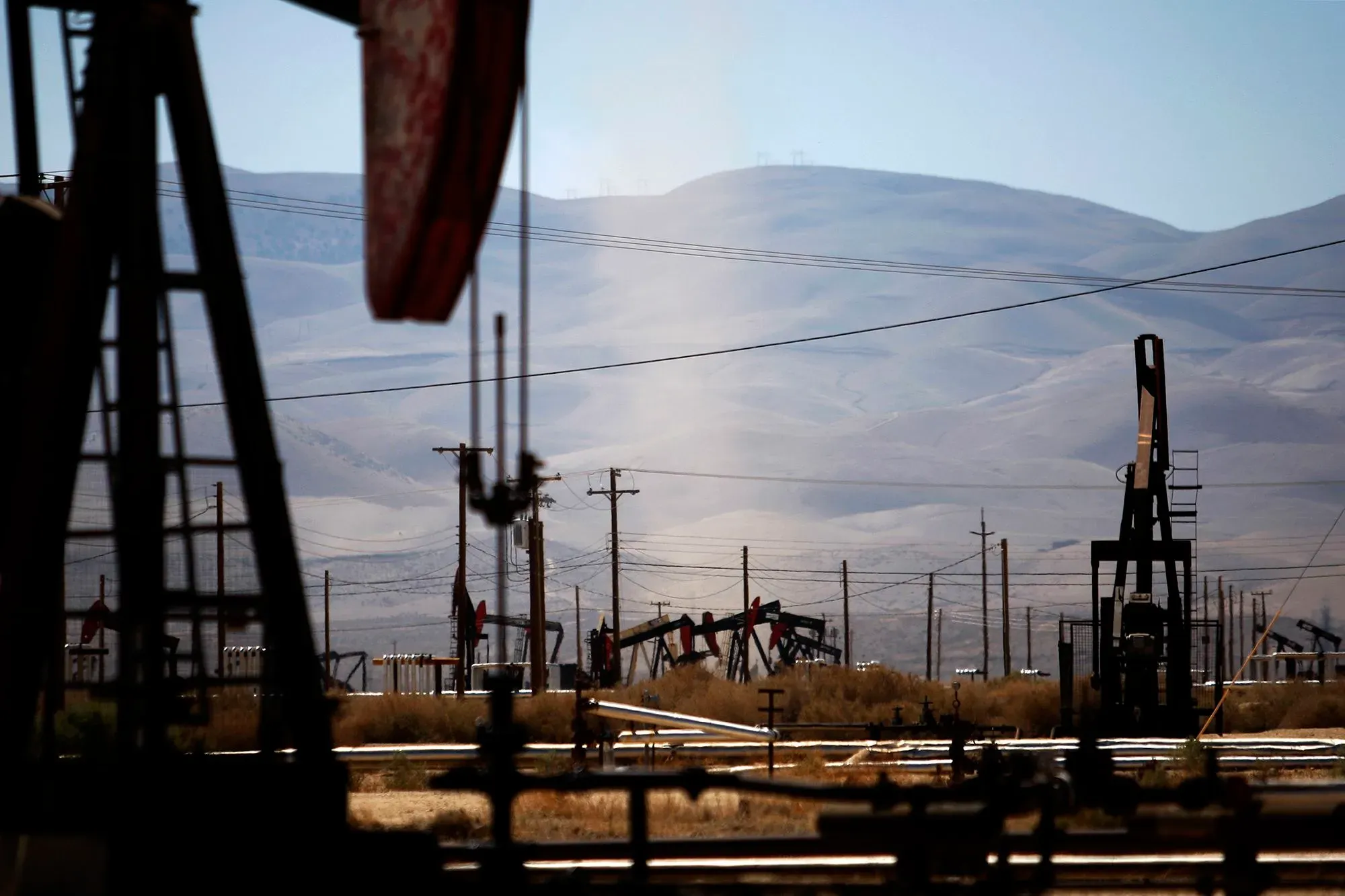 صورة لموقع استخراج النفط في الولايات المتحدة، تُظهر مضخات النفط في حقل نفطي مع جبال في الخلفية، تعكس تأثيرات الحرب الإيرانية على أسعار الوقود.