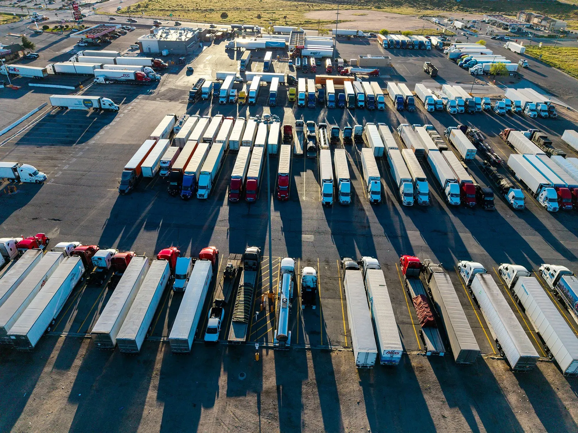 صورة جوية لموقف شاحنات مزدحم، يظهر مجموعة من الشاحنات الكبيرة المتوقفة بشكل منظم، تعكس تحديات صناعة النقل بالشاحنات في ظل ارتفاع أسعار الوقود.