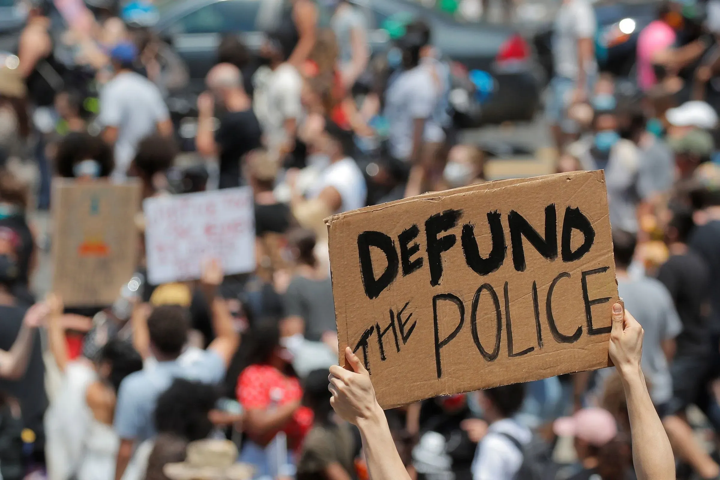لافتة تحمل عبارة "إلغاء تمويل الشرطة" وسط حشد من المتظاهرين، تعبر عن دعوات لإصلاحات في نظام العدالة الجنائية.