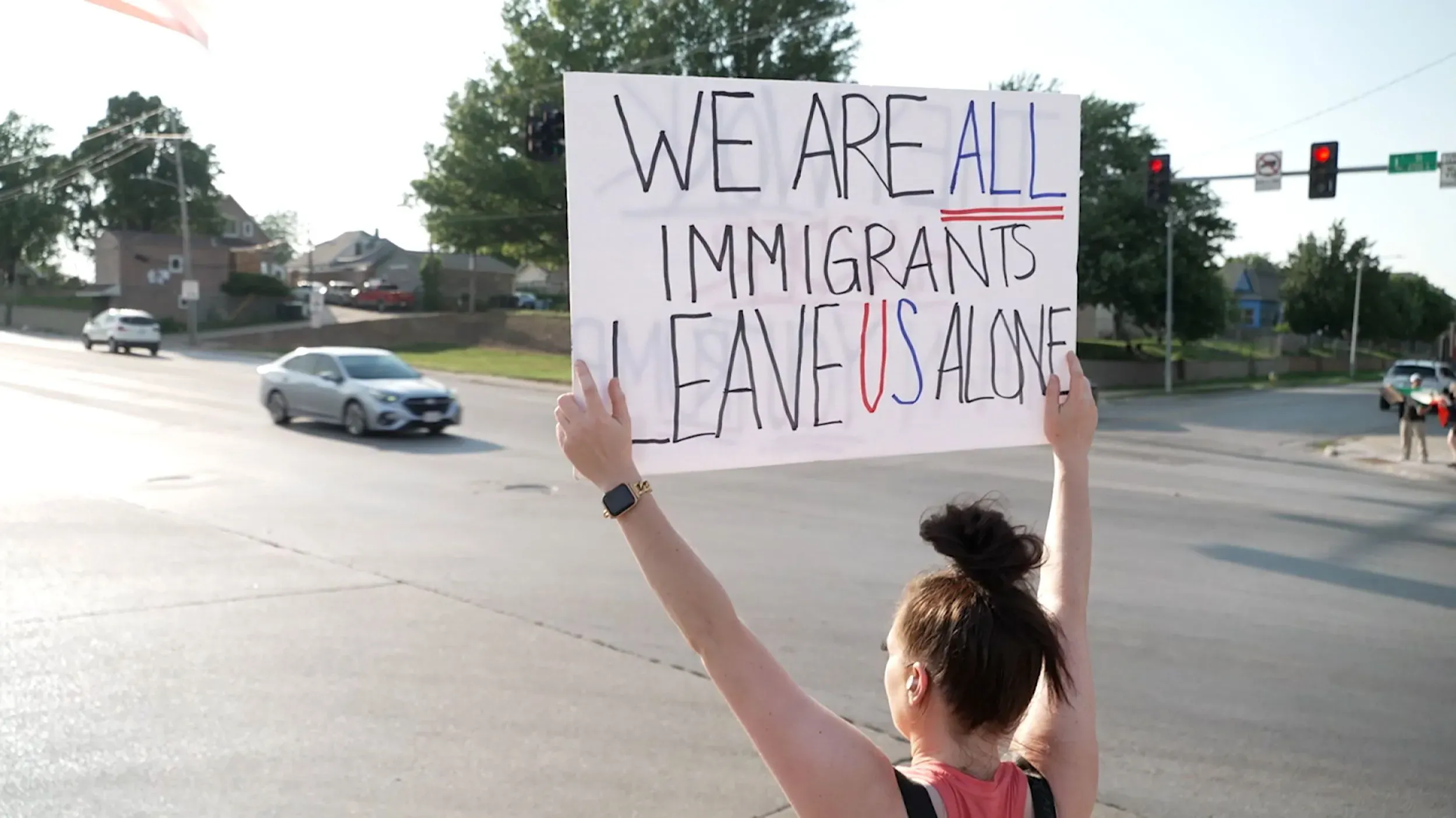 امرأة تحمل لافتة مكتوب عليها "نحن جميعًا مهاجرون اتركونا وحدنا"، تعبر عن دعمها للمهاجرين في نبراسكا وسط تزايد التوترات حول الهجرة.