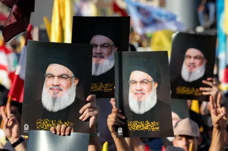 محتجون يحملون صور حسن نصر الله خلال إحياء ذكرى اغتياله، مع تواجد أعلام حزب الله في الخلفية، يعكس دعمهم المستمر.