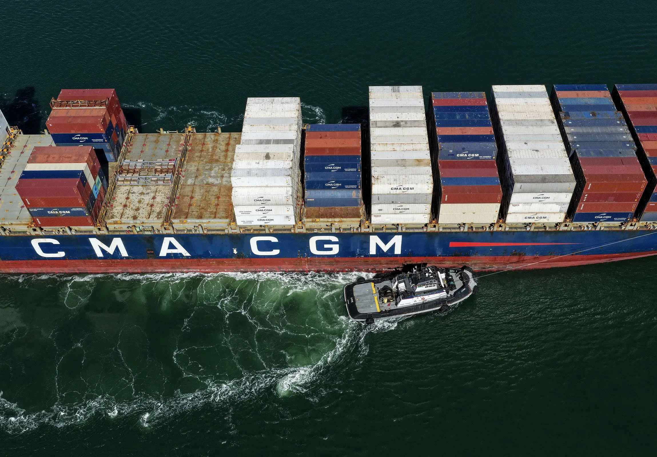 سفينة شحن تحمل حاويات متعددة الألوان، تبحر عبر المياه، تعكس تأثير التعريفات الجمركية على أسعار السلع المستوردة مثل القهوة.