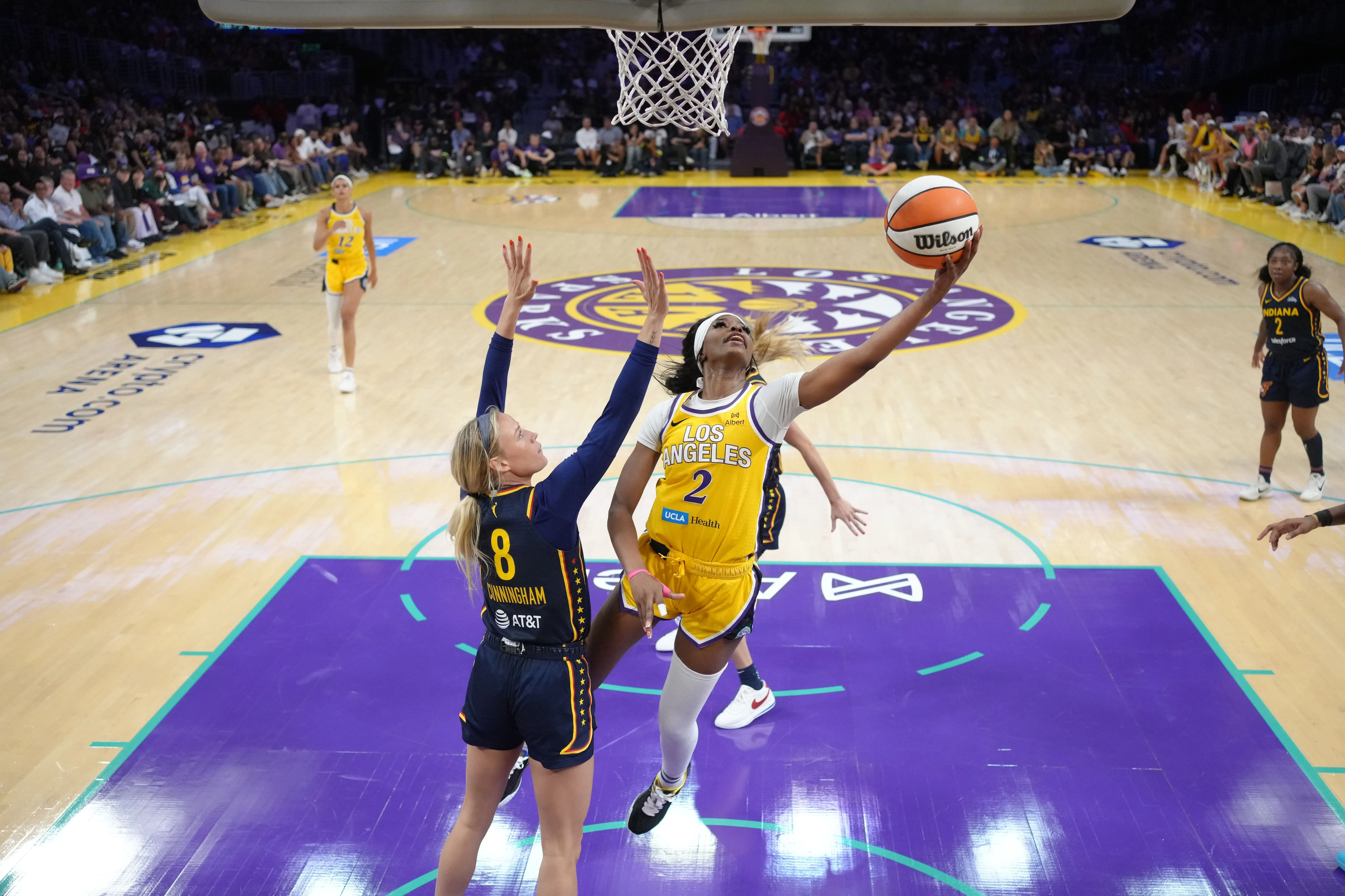 لاعبة كرة سلة من فريق لوس أنجلوس سباركس تسجل نقطة بينما تحاول حارسة فريق إنديانا فيفر صد الكرة، وسط أجواء حماسية في الملعب.