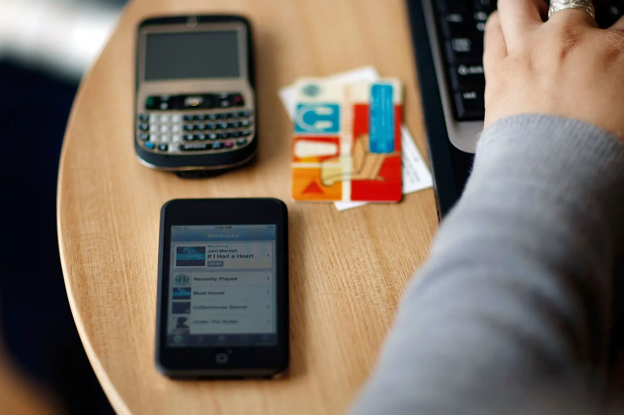 صورة تُظهر جهاز آي بود مع هاتف قديم وقطع بطاقات ائتمان على طاولة، تعكس تحول Apple من الموسيقى إلى الهواتف الذكية.