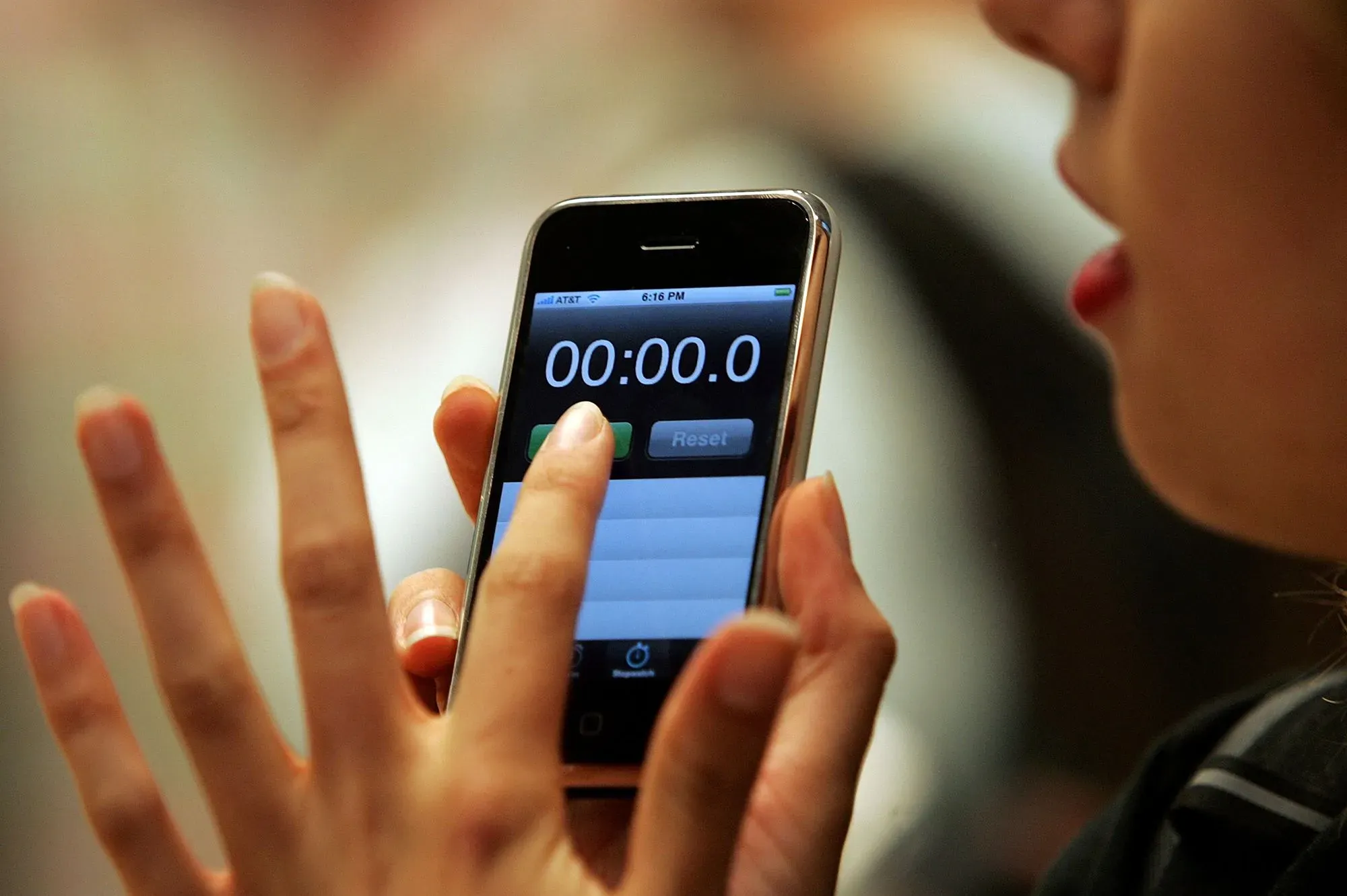 شخص يستخدم هاتف آيفون الأول، مع عرض شاشة التوقيت، مما يعكس الابتكار التكنولوجي الذي قدمته آبل في عالم الهواتف الذكية.